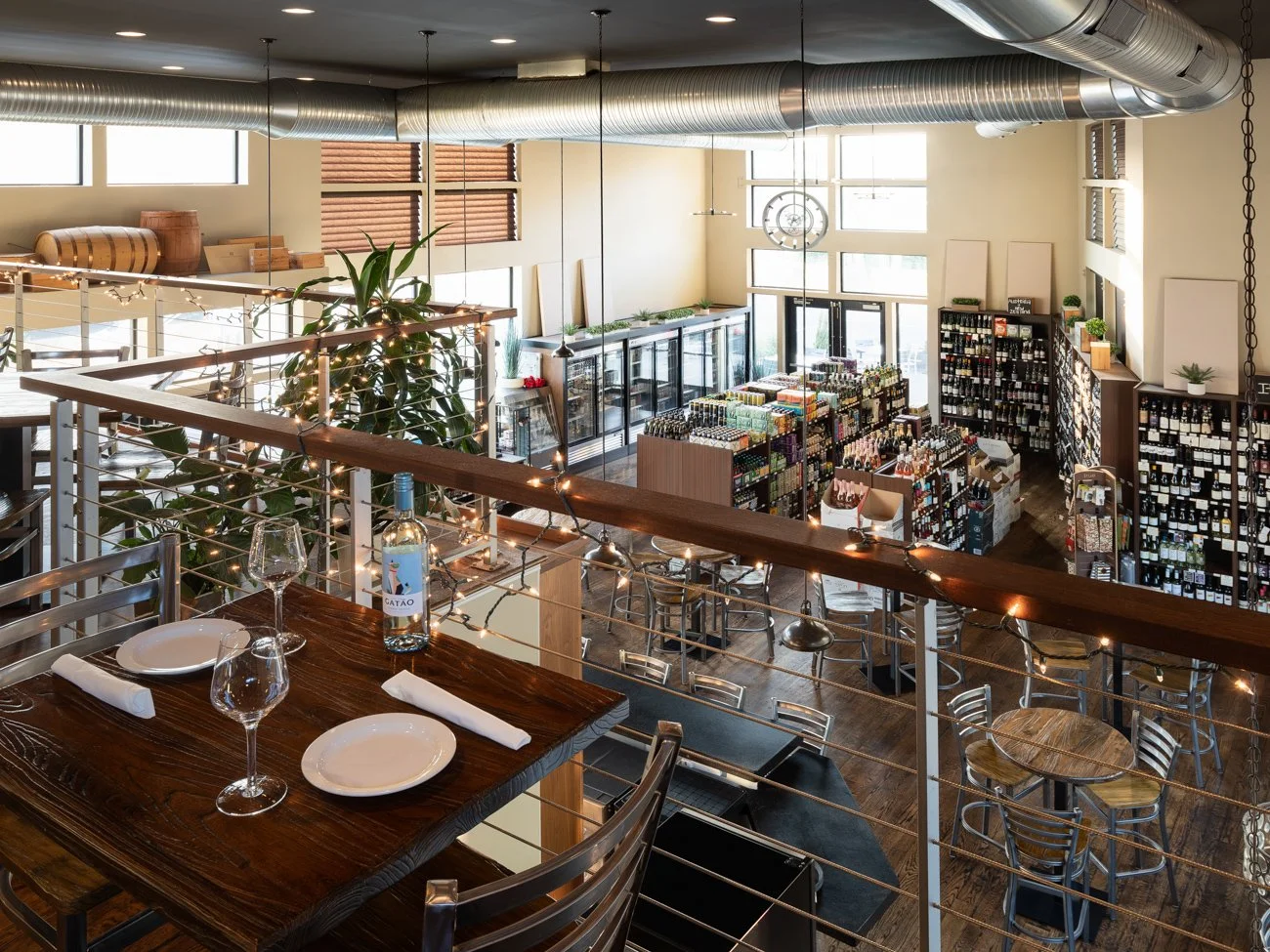 Inside a modern, well-lit restaurant with a wine display, tables set with plates and glasses, and decorative plants.