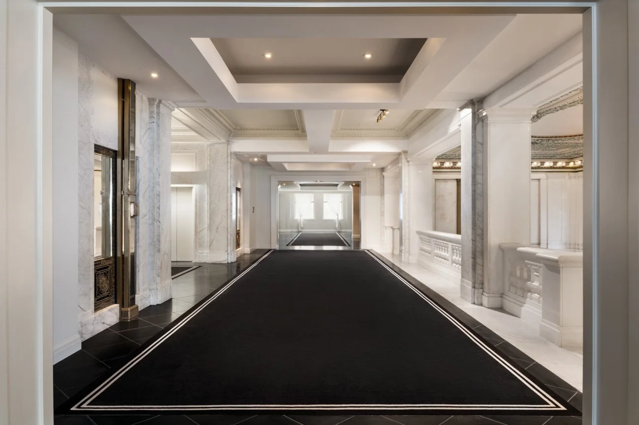 Elegant lobby with white marble columns, moldings, and a black carpeted floor.