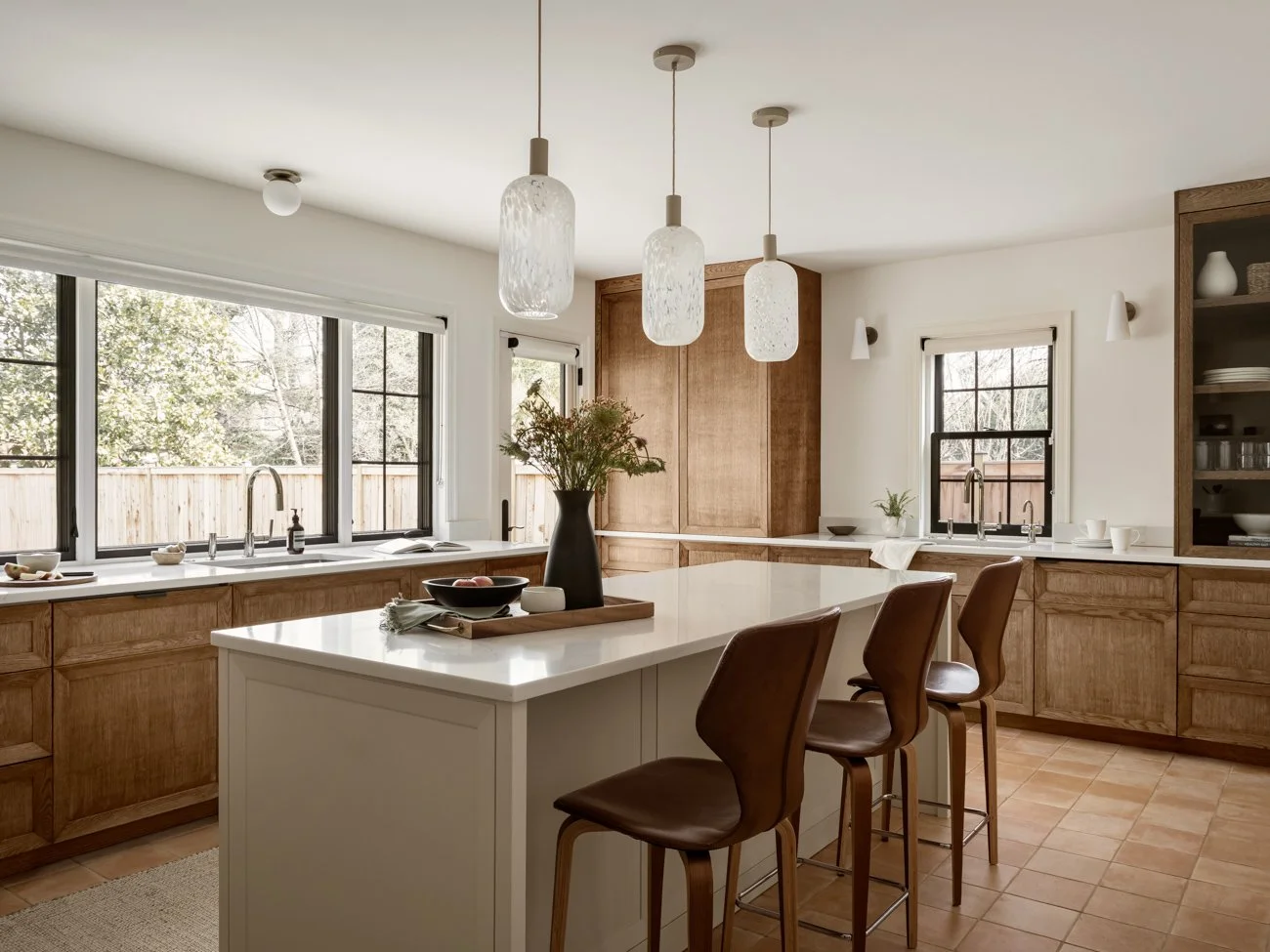 Modern kitchen with wooden cabinets, white countertops, and three pendant lights over an island with brown chairs.