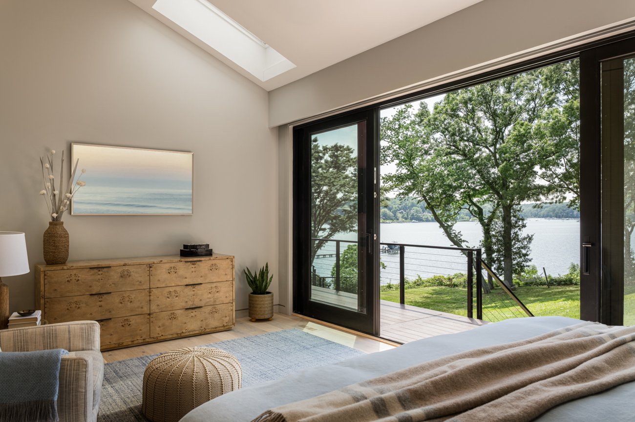 Living room with a large sliding glass door leading to a balcony overlooking a lake with trees.
