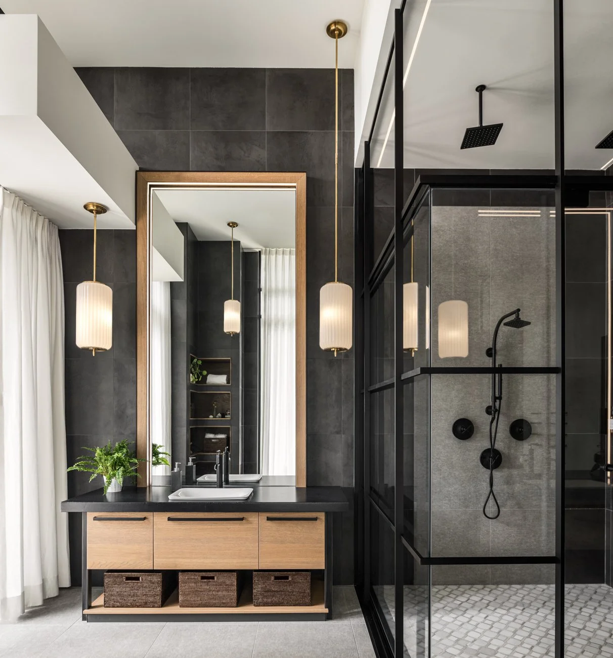 Modern bathroom with black and wood accents, featuring a vanity with two sinks, a large mirror, pendant lighting, and a glass-enclosed shower with black fixtures.