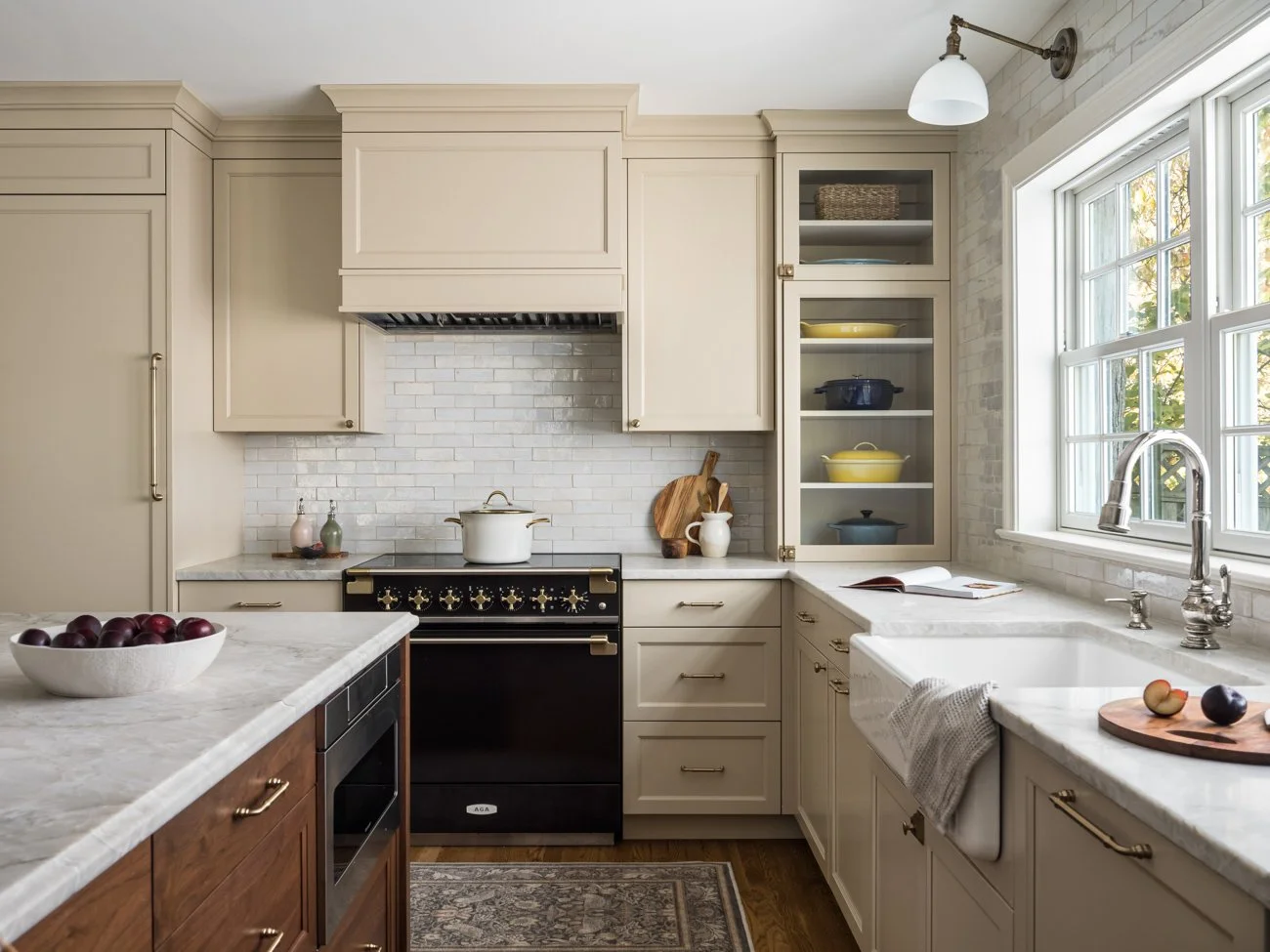 Kitchen with cream-colored cabinets, a black stove, open shelves with yellow and blue dishes, a window above the sink, and a bowl of cherries on the island.