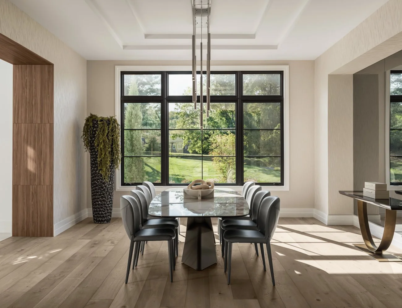Modern dining room with large window, marble table, black chairs, wood and neutral decor, and outdoor view.