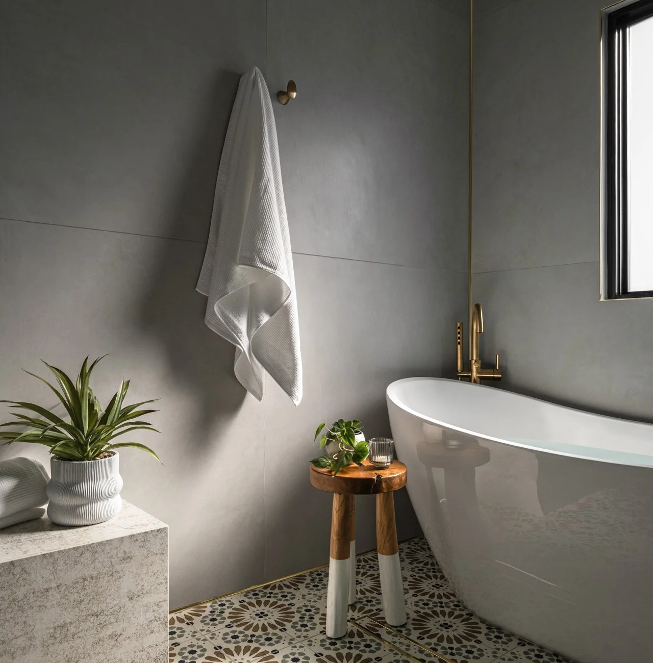 Modern bathroom with a white freestanding bathtub, a small wooden stool, indoor plants, and a wall-mounted white towel.