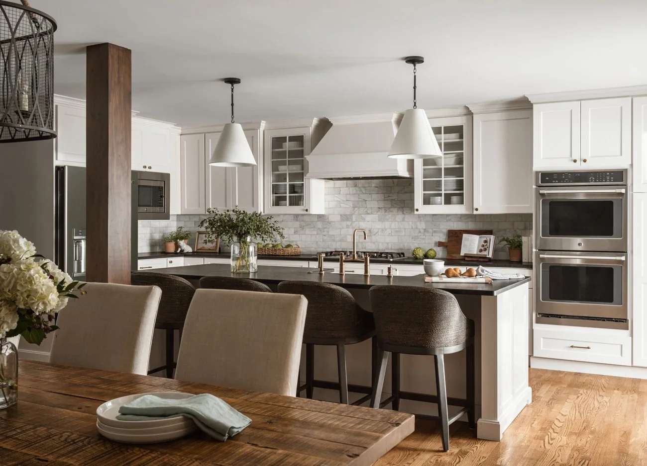 Modern kitchen with white cabinets, black countertop island, stainless steel appliances including double oven and microwave, and pendant lighting.