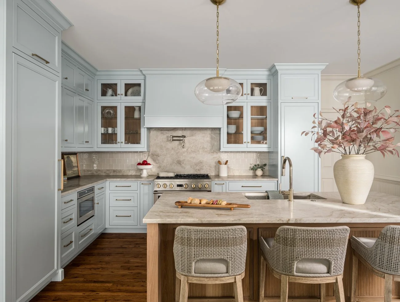 Modern kitchen with light blue cabinets, a marble island, and a vase with pink leaves.