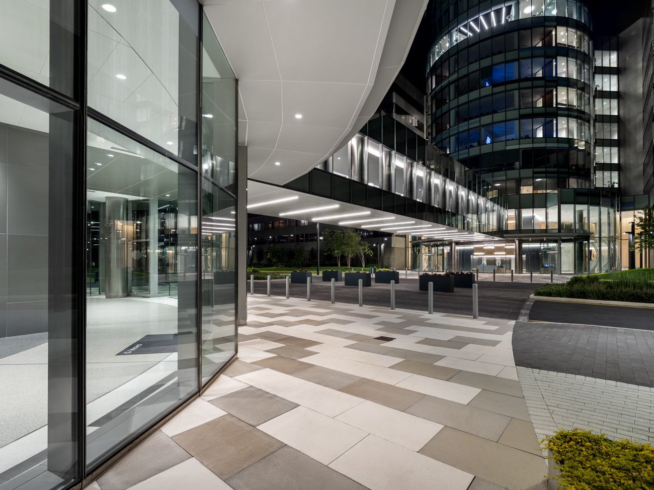 Night view of a modern glass office building with well-lit entrance and surrounding landscaped area.