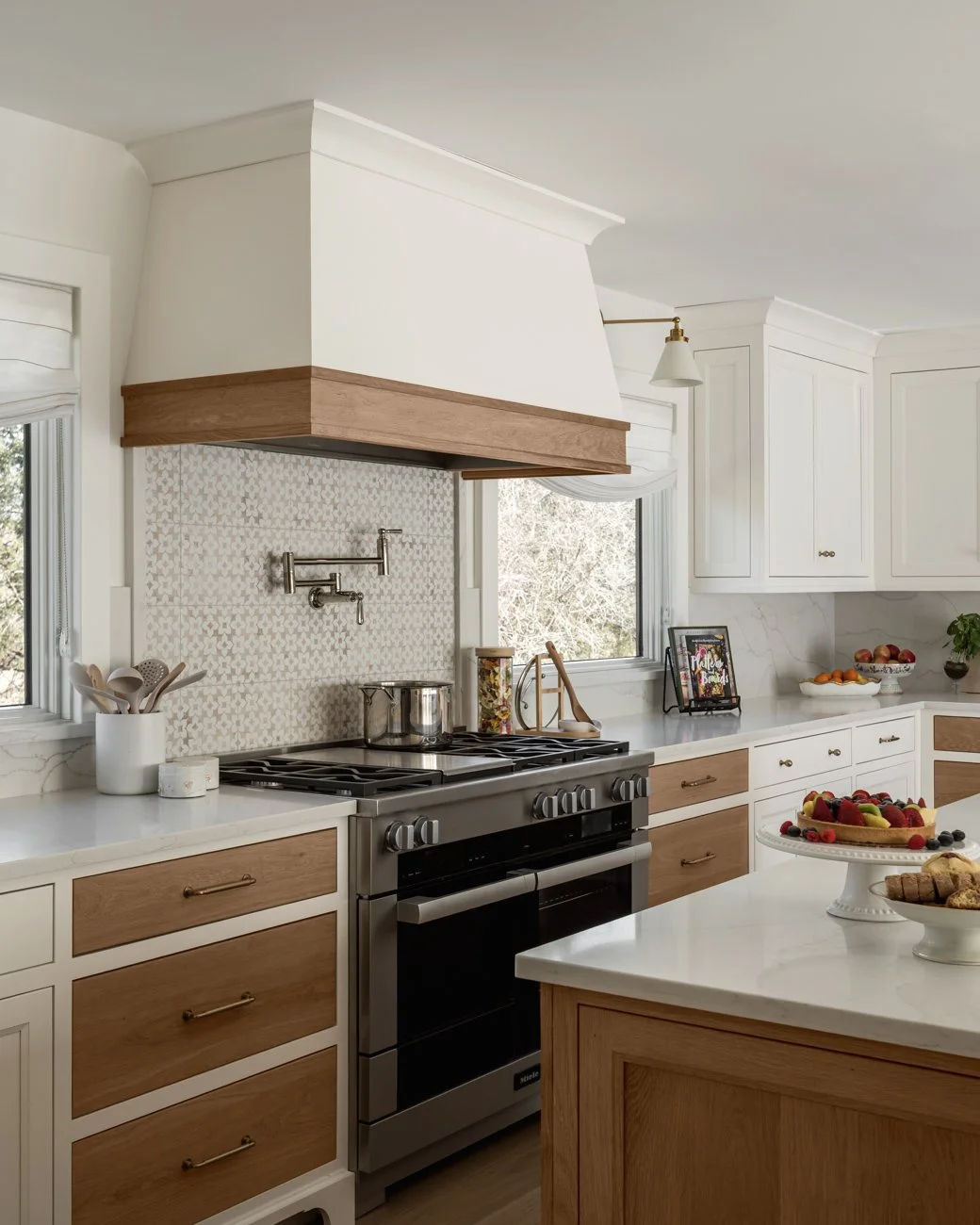 Modern kitchen with white cabinets, wooden accents, stainless steel stove, marble countertops, and fruit decorations.