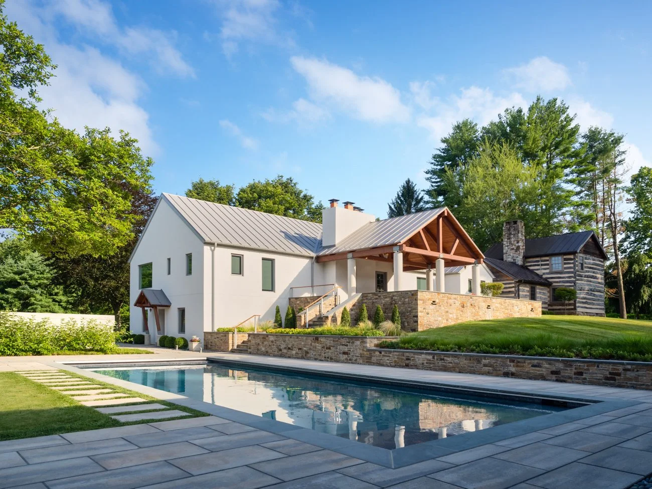 Modern house with a pool, landscaped yard, and mature trees under a partly cloudy sky.