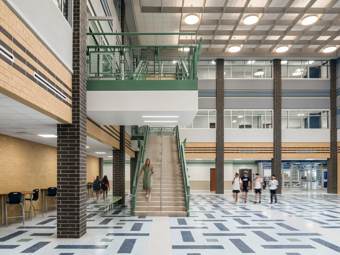 Interior of a school or university building lobby with students walking and stairs leading to upper floors.