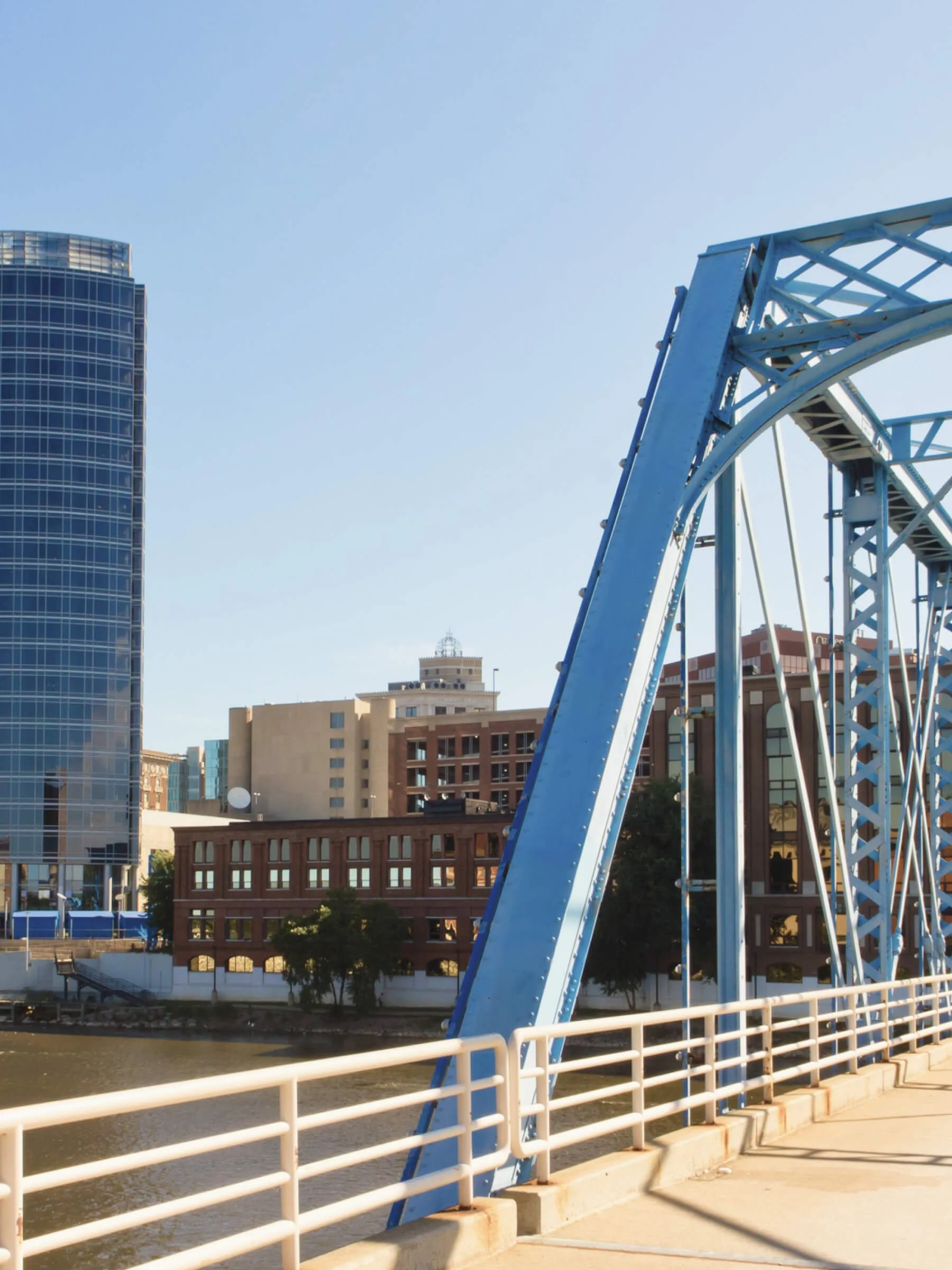 A blue steel bridge over a river with modern buildings in the background.