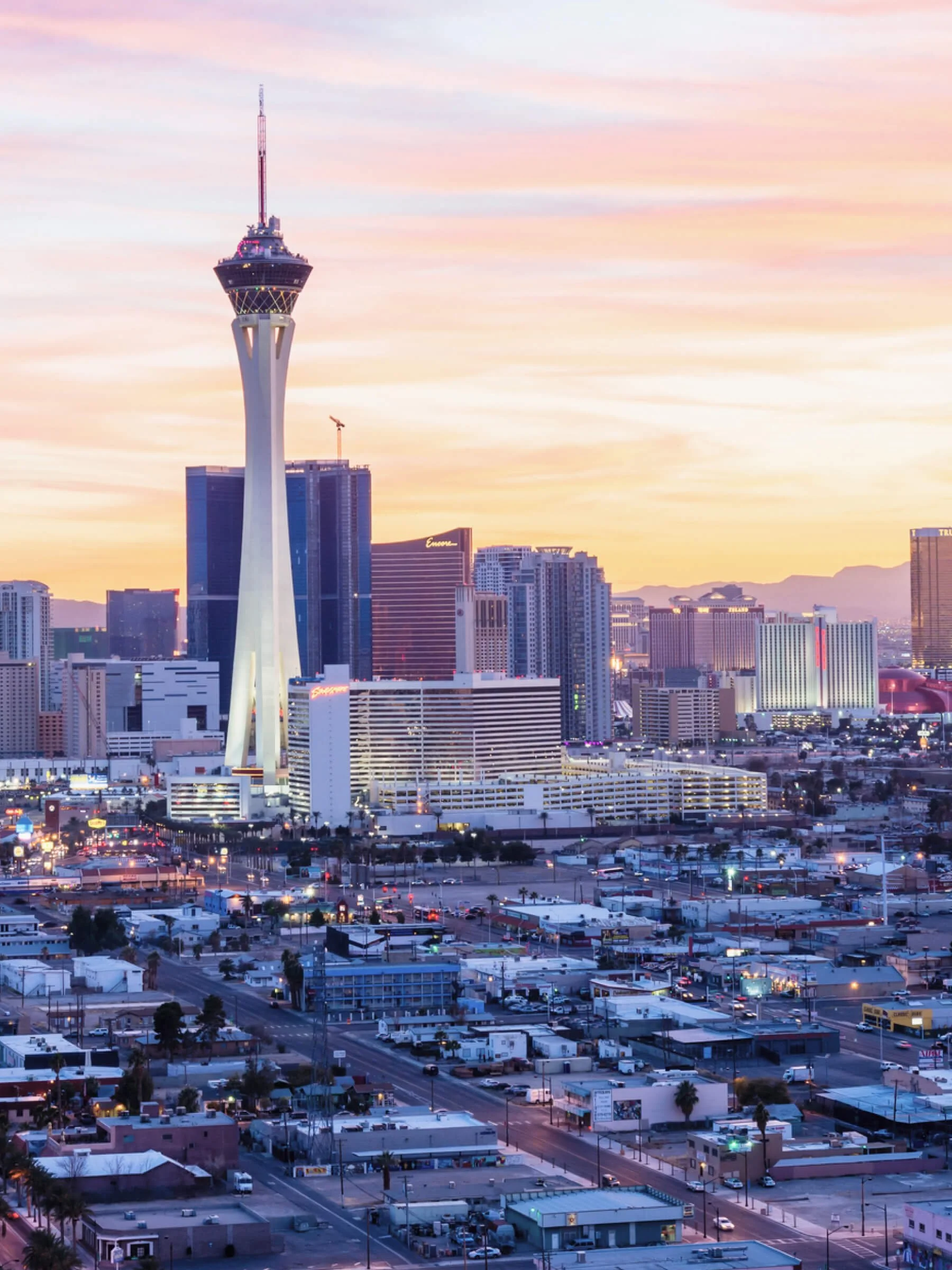 Las Vegas skyline at sunset with the Stratosphere Tower in the foreground and various high-rise buildings in the background.