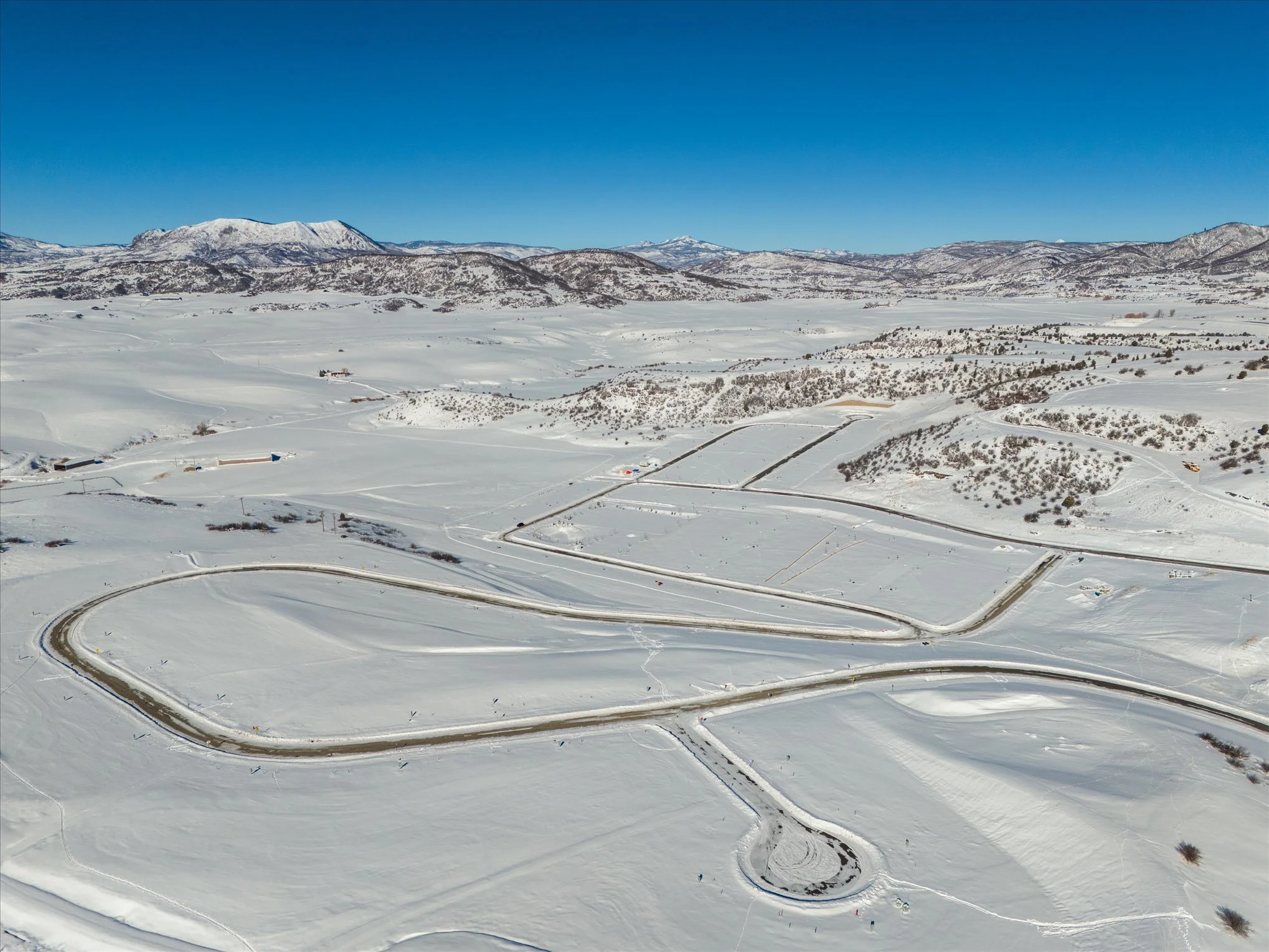 Aerial view of a snow-covered landscape with a winding road and mountains in the background.