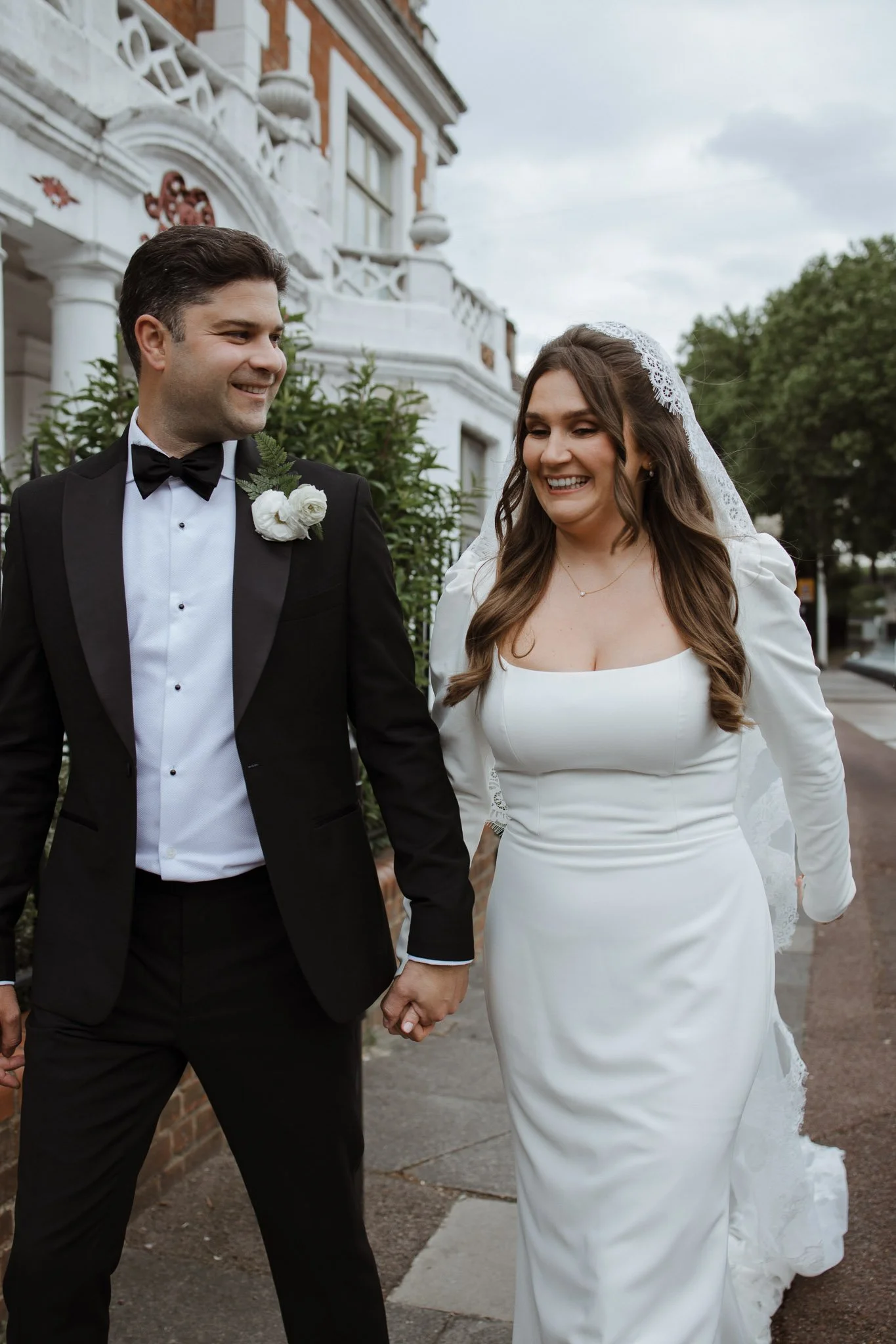 Happy bride and groom walking hand in hand outside a building on their wedding day.