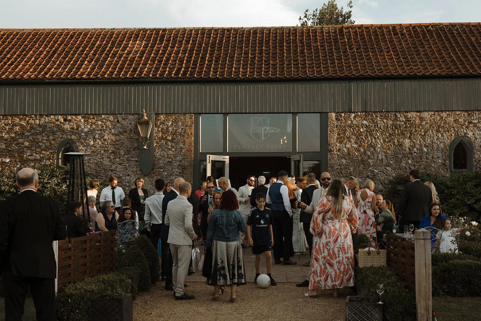 A group of people gathered outside a rustic stone building with a sign that says 'Penney Abbey' above the entrance, celebrating an event during sunset.