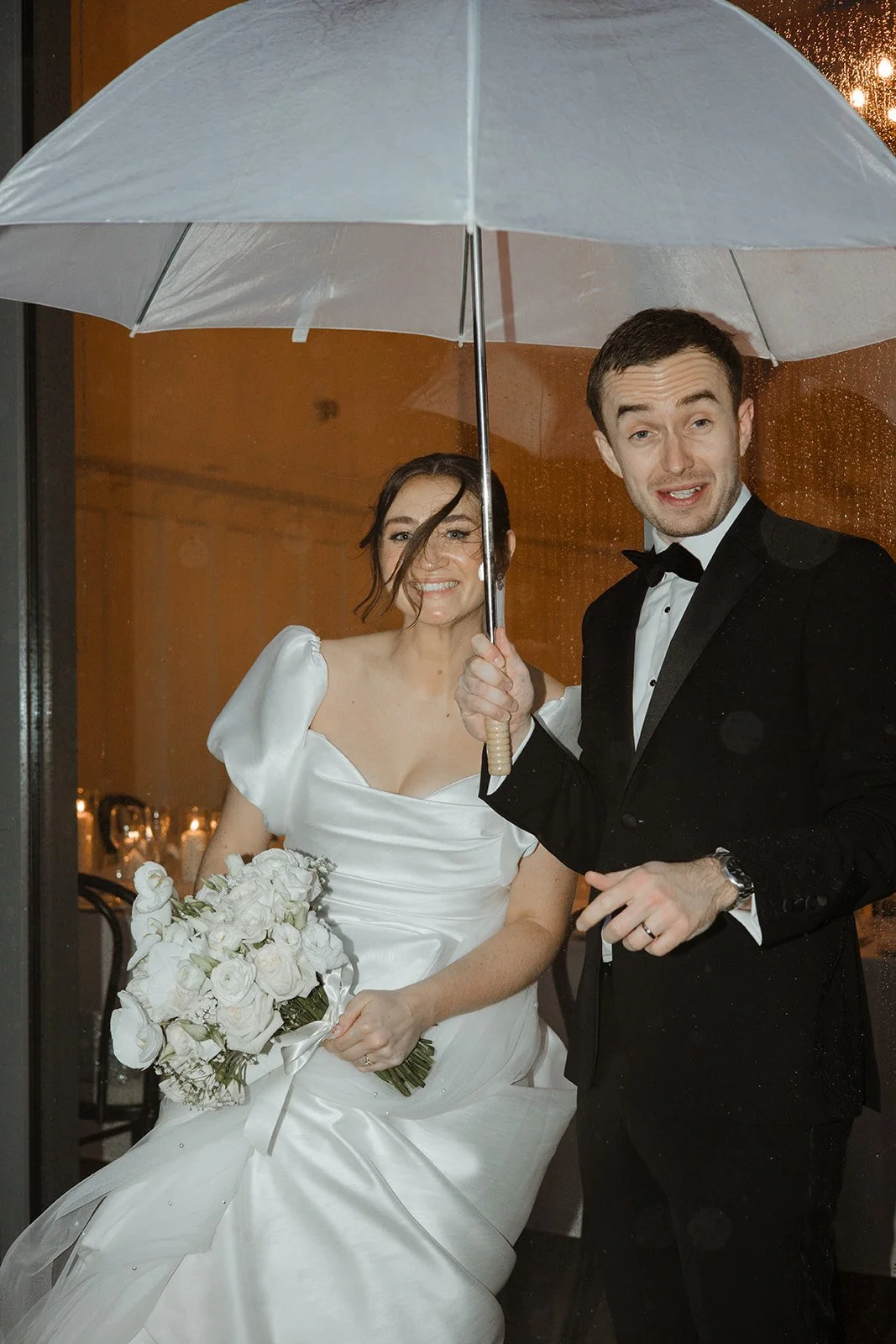 Newlywed couple standing with an umbrella during a wedding celebration.