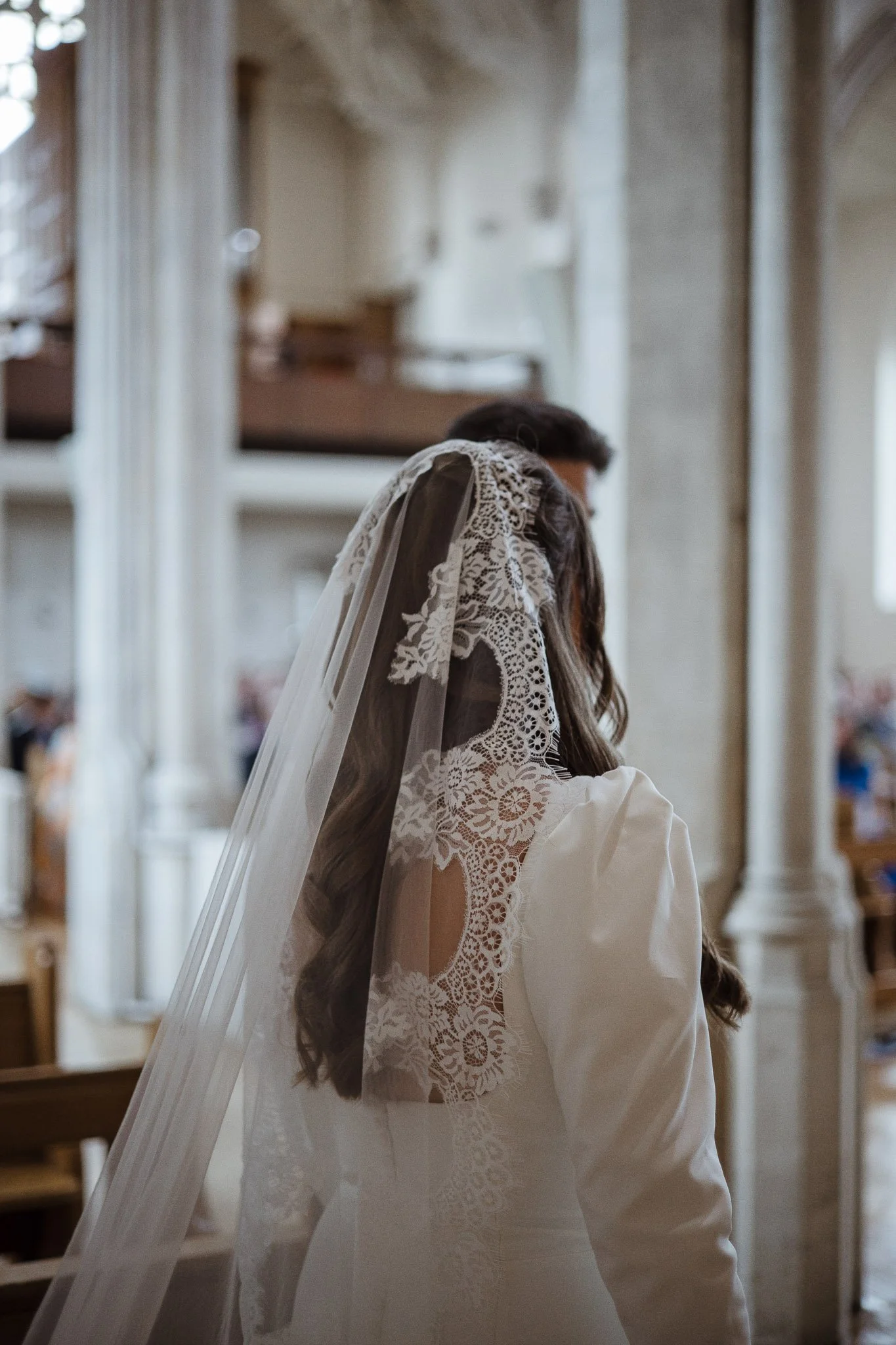 A bride with a lace veil and a white dress standing inside a church.