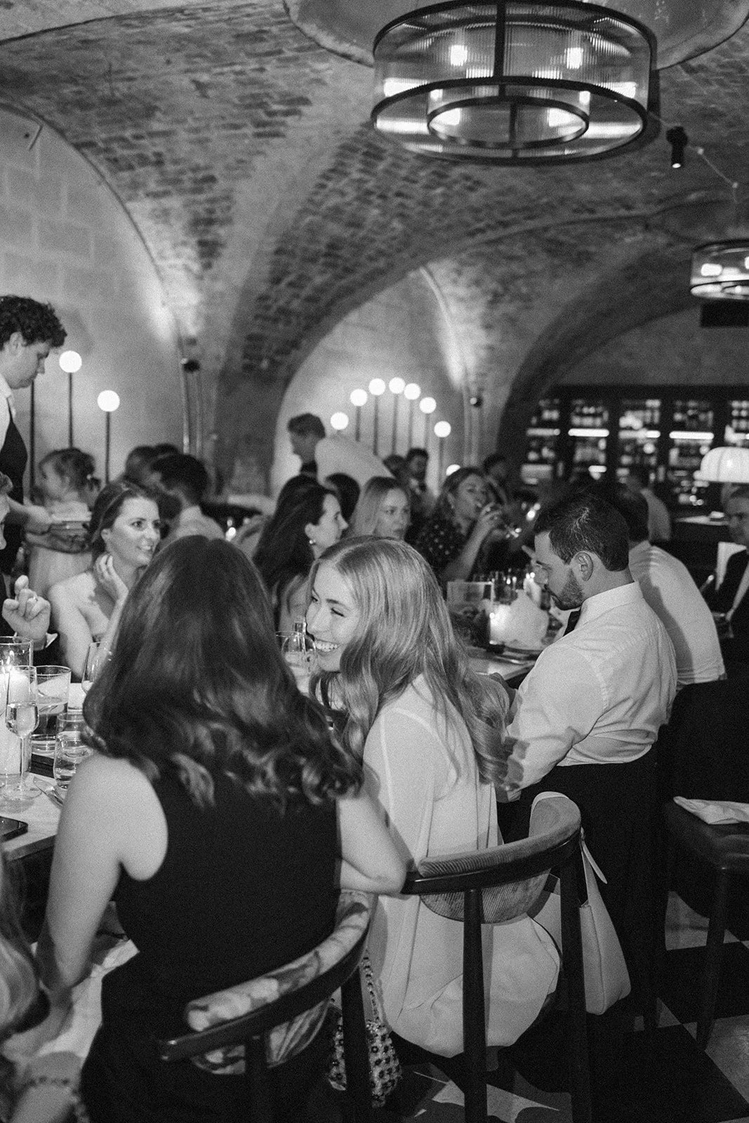 People dining in a dimly lit restaurant with brick arched ceilings and modern hanging lights, enjoying a social gathering.