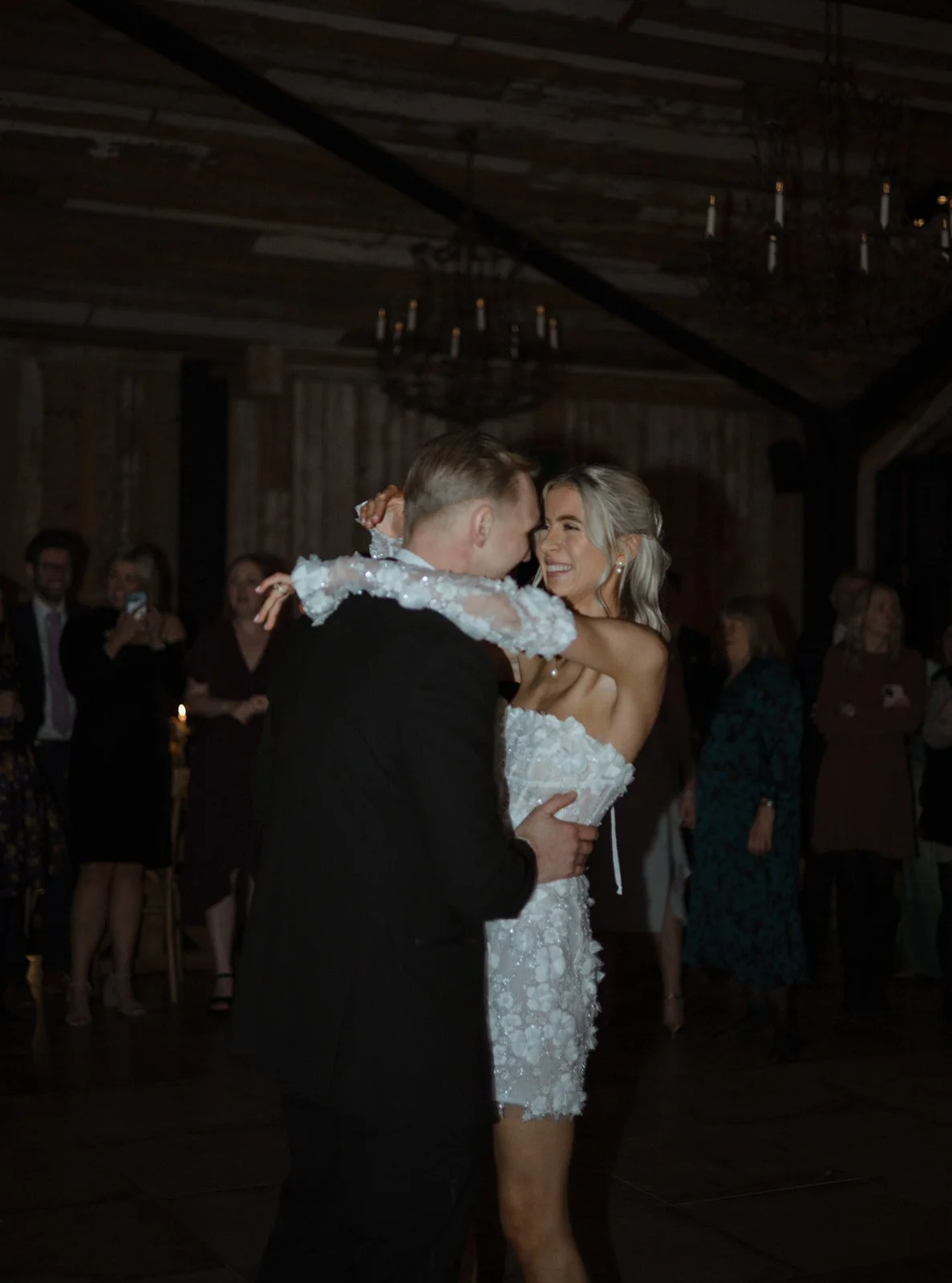 A bride and groom dancing at their wedding reception, surrounded by guests watching and taking photos.