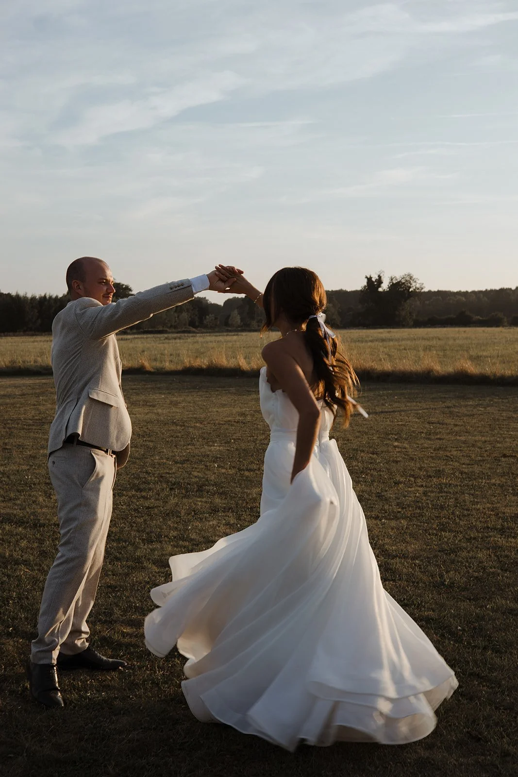 A couple dancing outdoors on a grassy field during sunset.