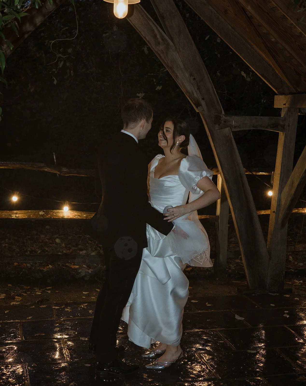 A bride and groom dancing in a dimly lit, rustic setting at night.