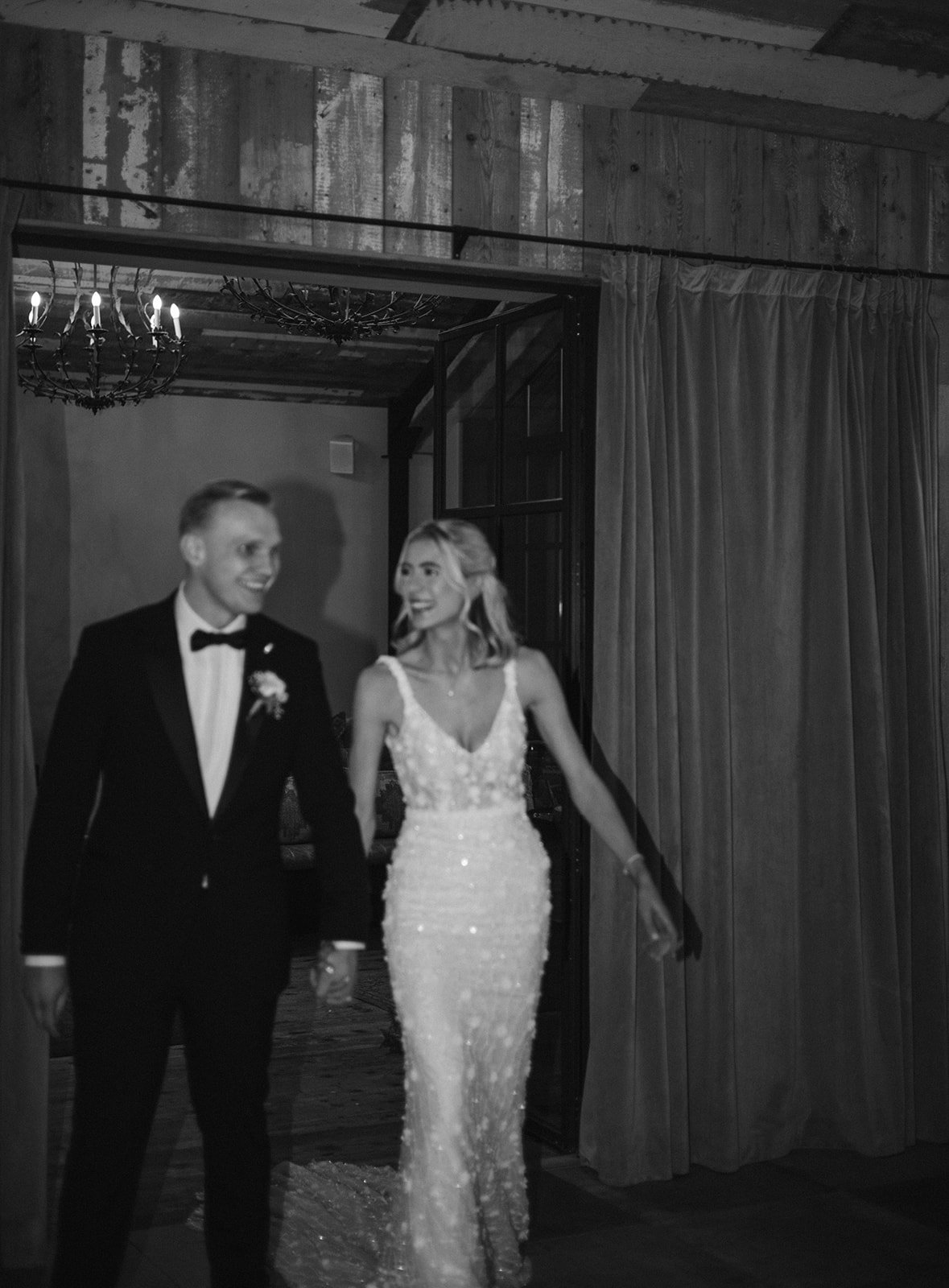 A bride and groom walking hand in hand at their wedding reception, smiling and looking at each other.