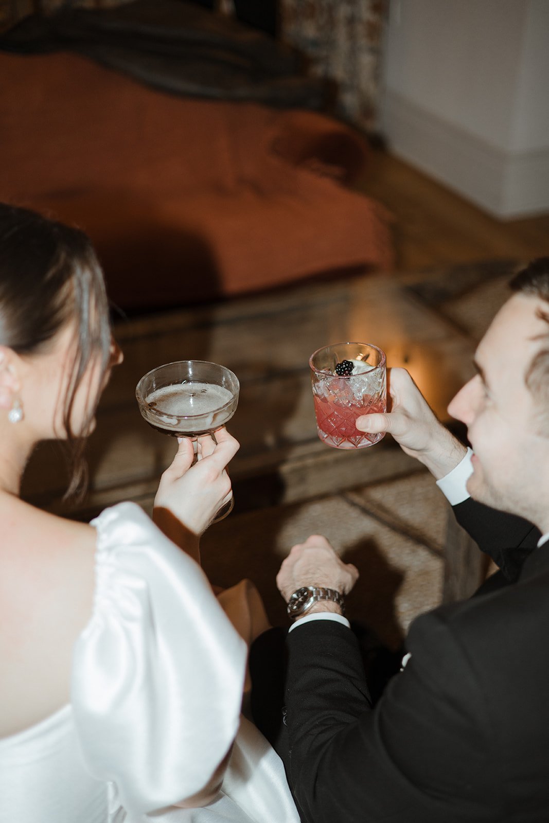 A woman in a white dress and a man in a tuxedo holding cocktails at a formal event.