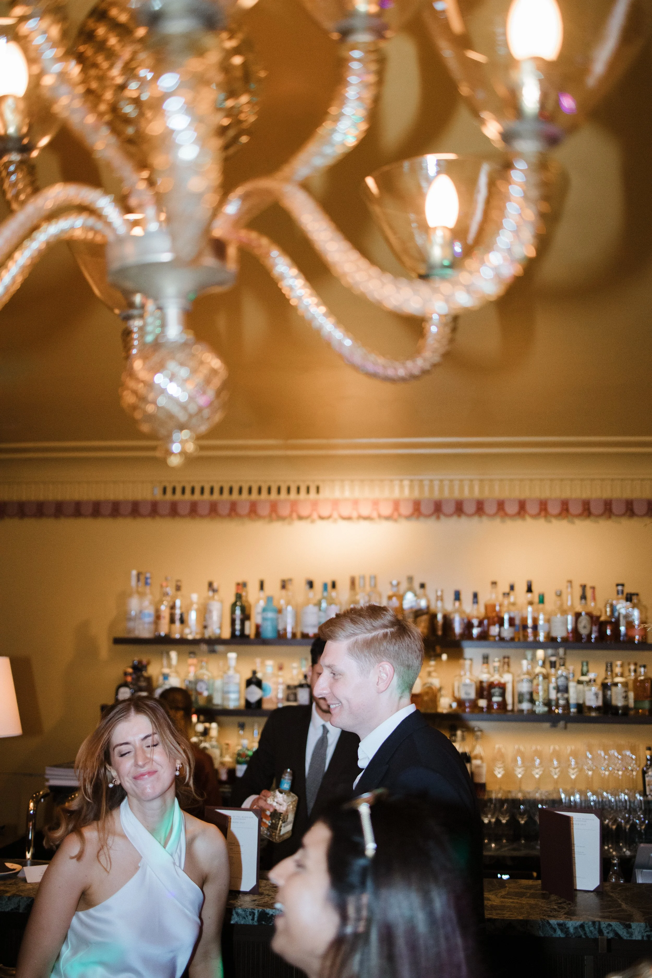 People socializing at a bar with a chandelier hanging from the ceiling.