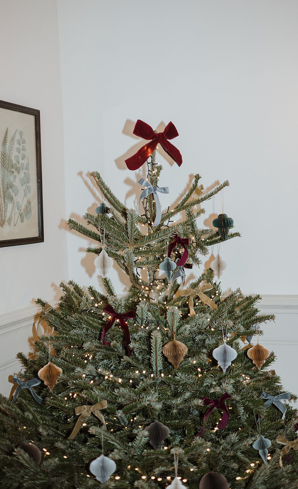 Decorated Christmas tree with ornaments, ribbons, and lights in a living room corner.