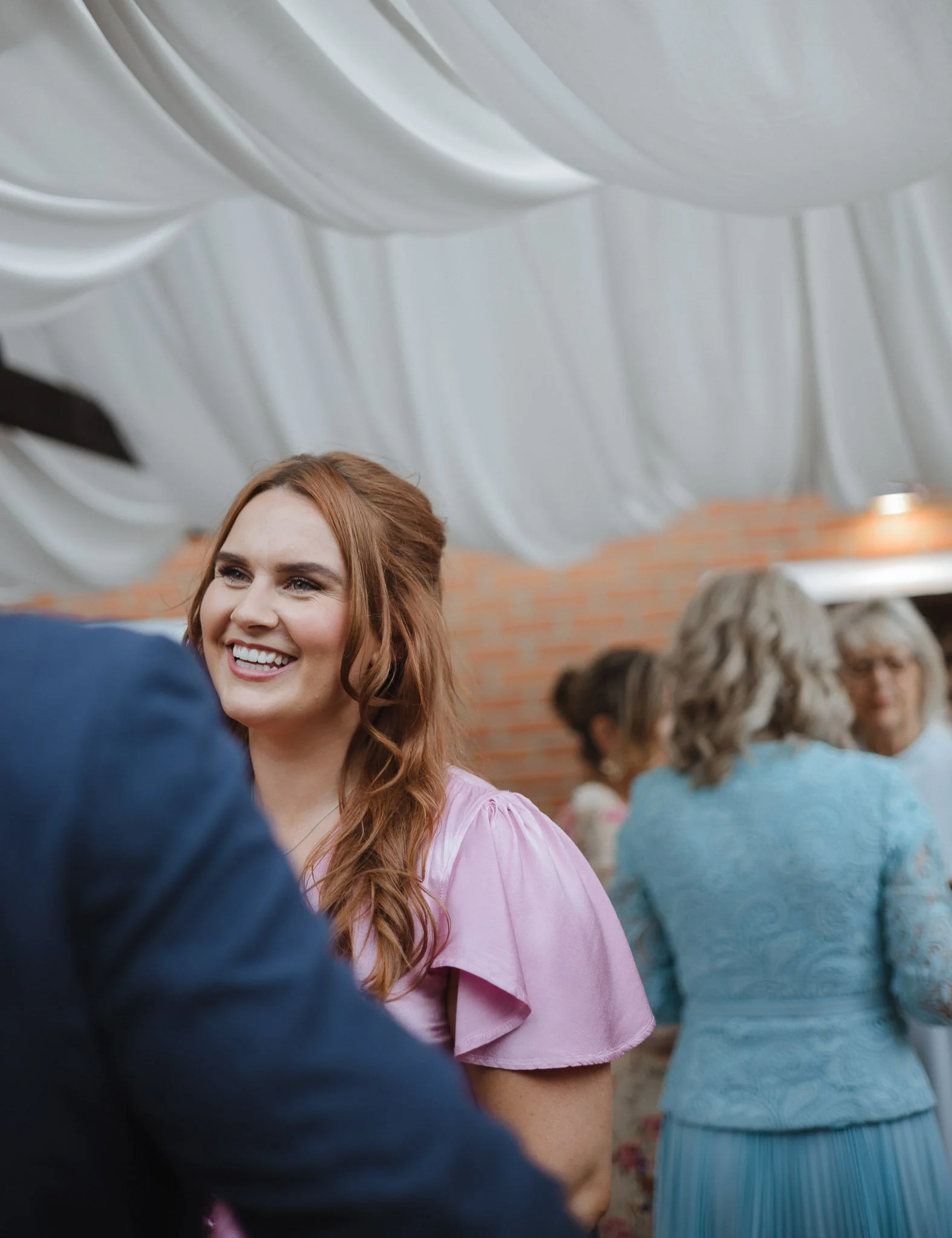 Smiling woman with long red hair wearing a pink dress at a social gathering.