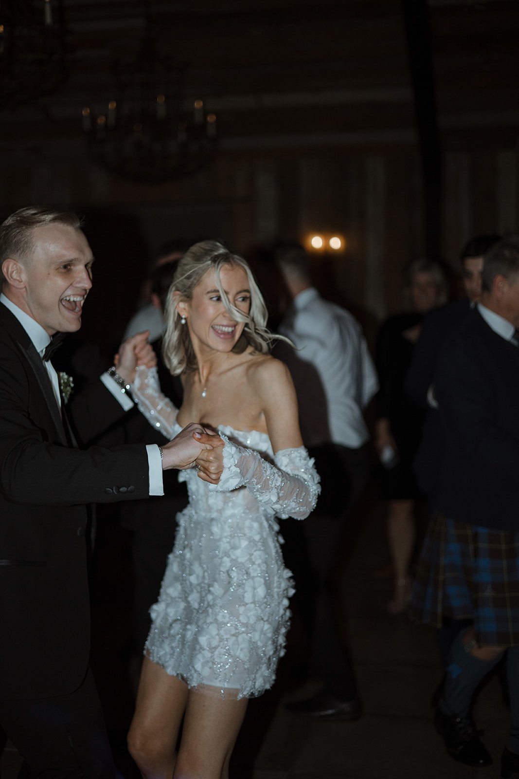 A bride and groom dancing at a wedding reception, surrounded by guests in a dimly lit room.