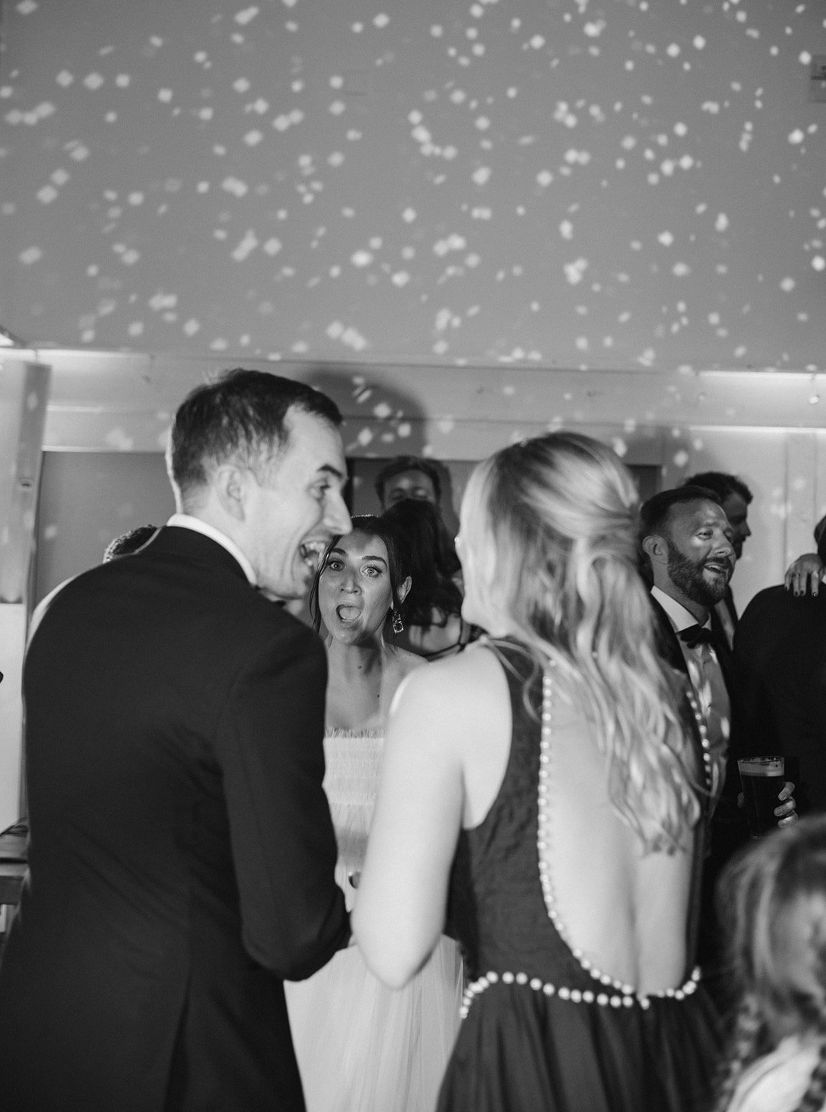 People dancing and celebrating at a wedding reception, with confetti falling from the ceiling.