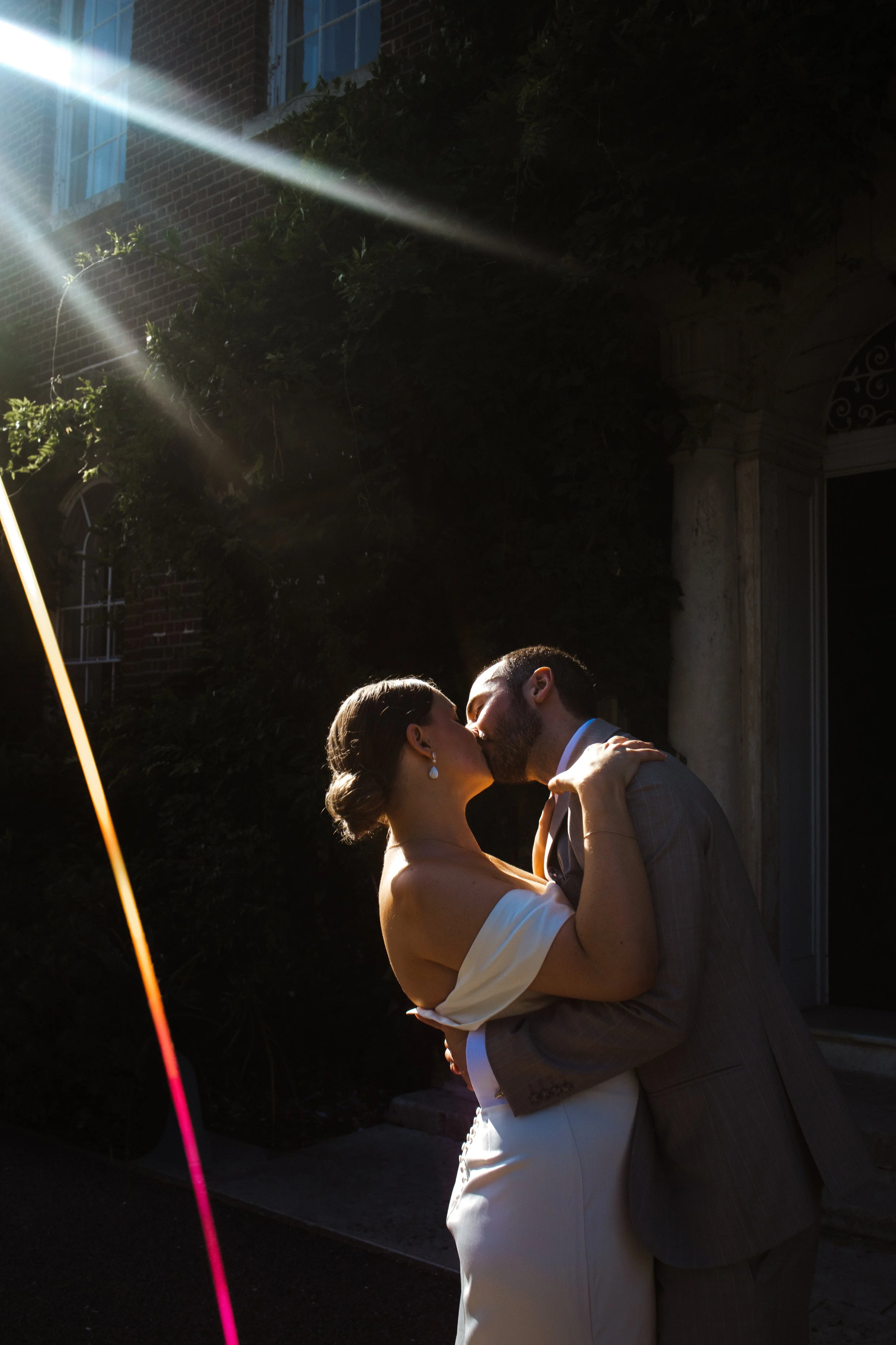 A couple wearing wedding attire sharing a kiss outside during sunset.