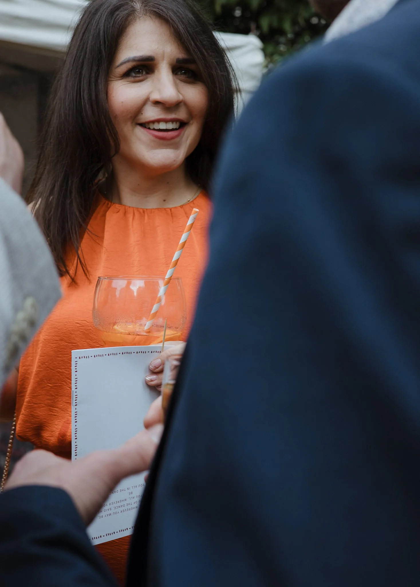 A woman smiling while holding a drink with a striped straw at an outdoor gathering.