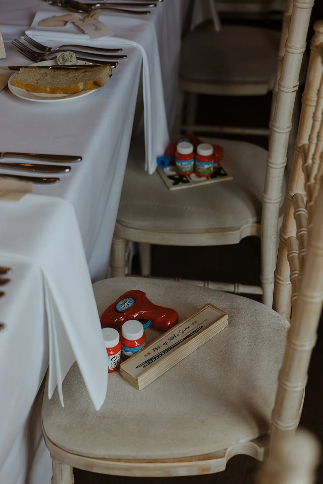 A table set with silverware, a plate with bread, and a chair with a red toy phone, bottles of medicine, and a wooden sign that reads 'Pick Up Sticky Game'.
