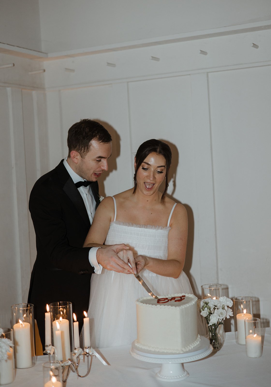 Newlyweds cutting a wedding cake, surrounded by candles and flowers.