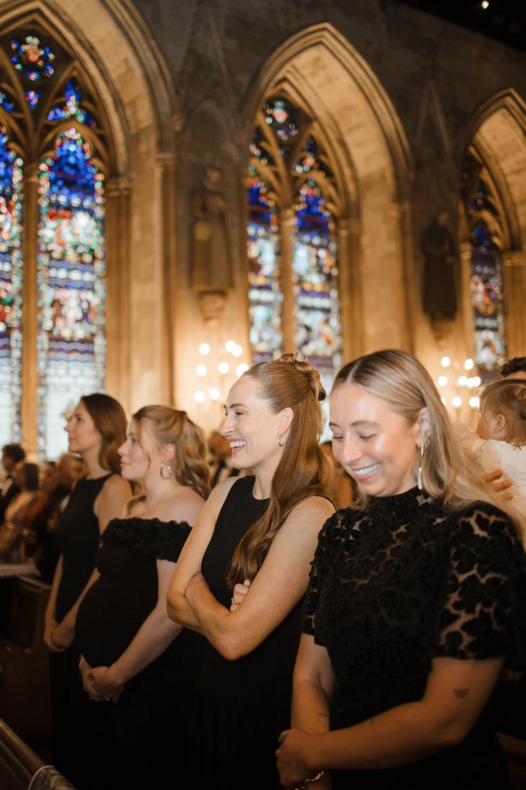 Group of women in black dresses attending a church service inside a Gothic cathedral with stained glass windows and warm lighting.