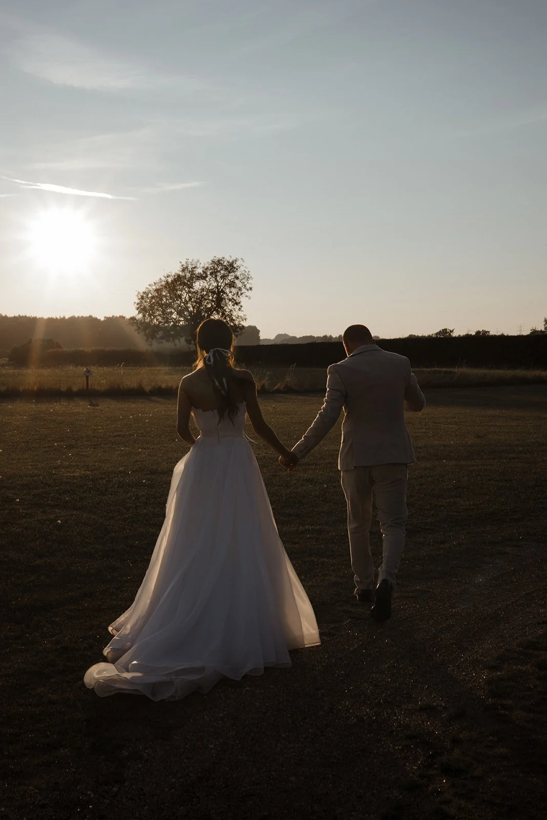 A bride and groom holding hands walking outdoors during sunset in a natural landscape.