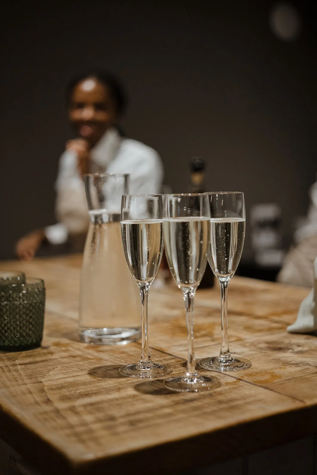 Three flutes of champagne on a wooden table with a blurred person in the background.