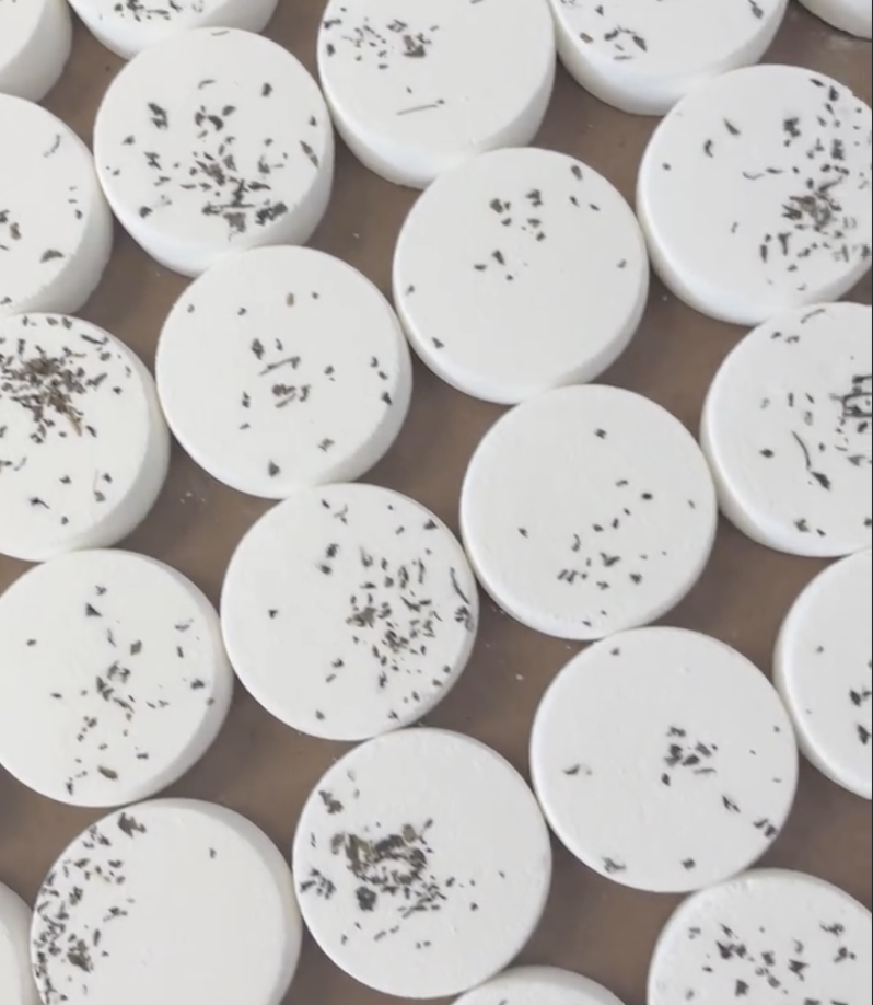 Multiple round white bath bombs with black speckles on a brown surface.