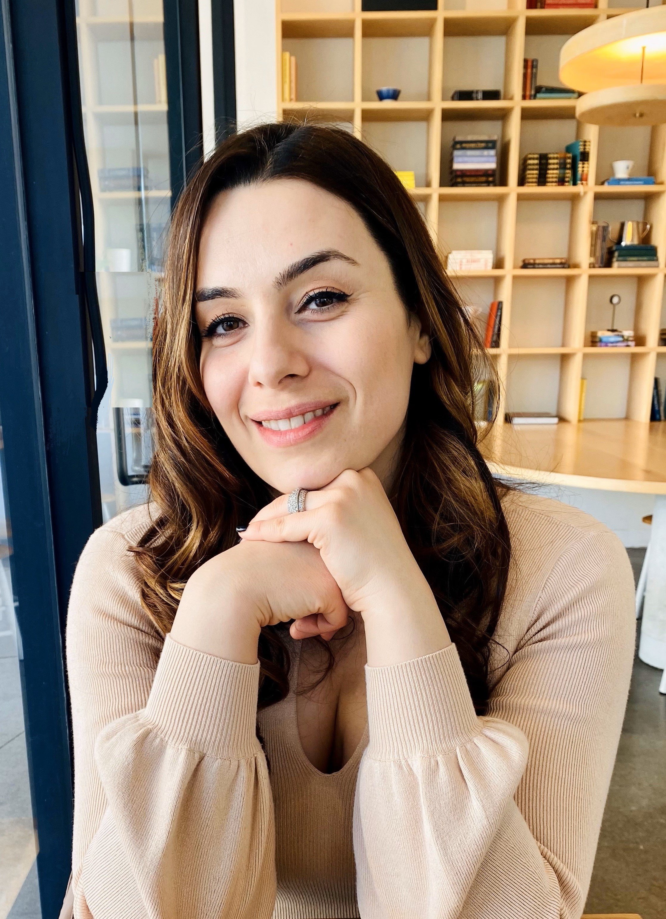 Woman smiling indoors with bookshelves in the background.