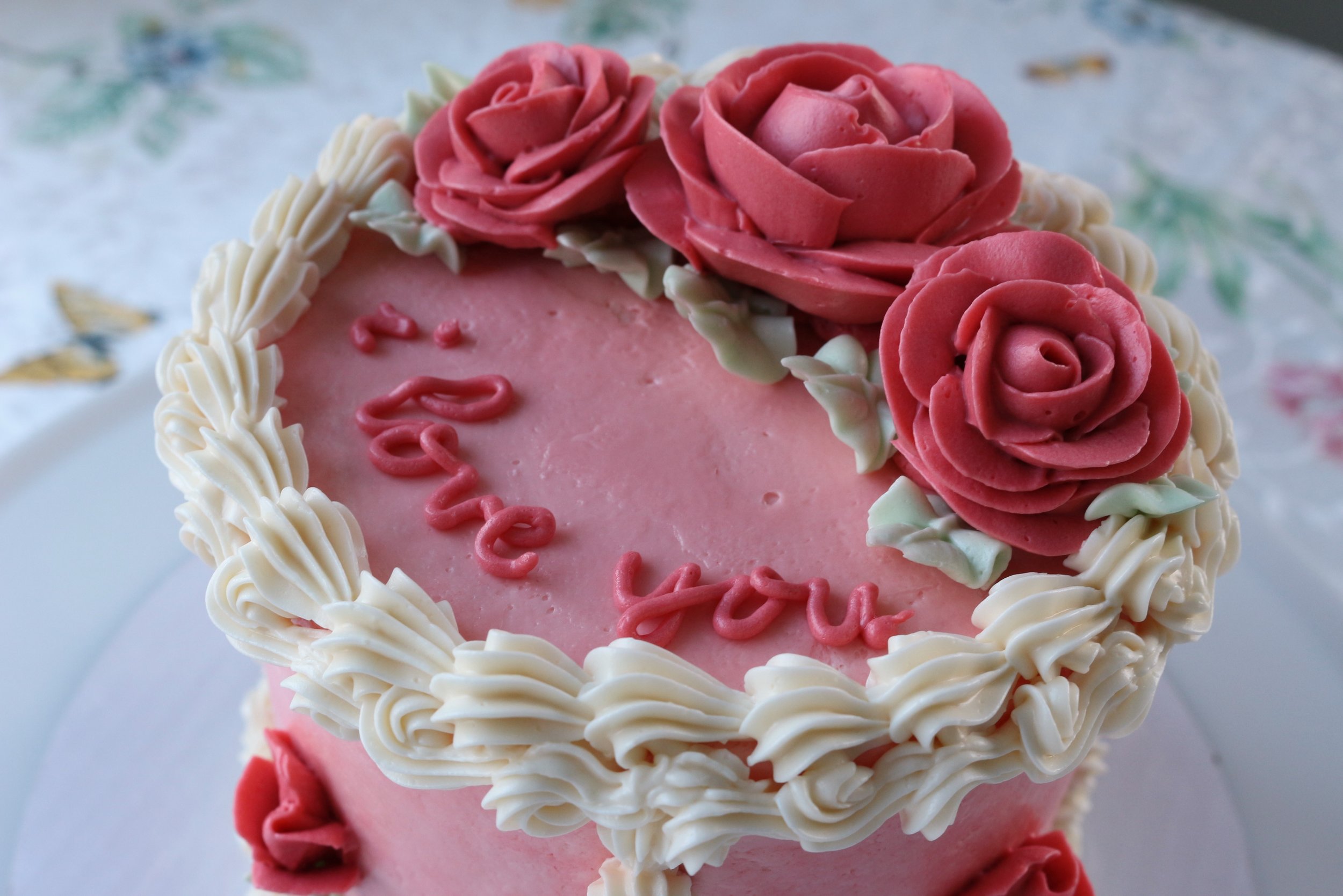 Side top view of cake with piped writing and three roses. Shell and reverse shell borders. Vintage piping on a Valentine's Day Cake. Cakes by Caroline.