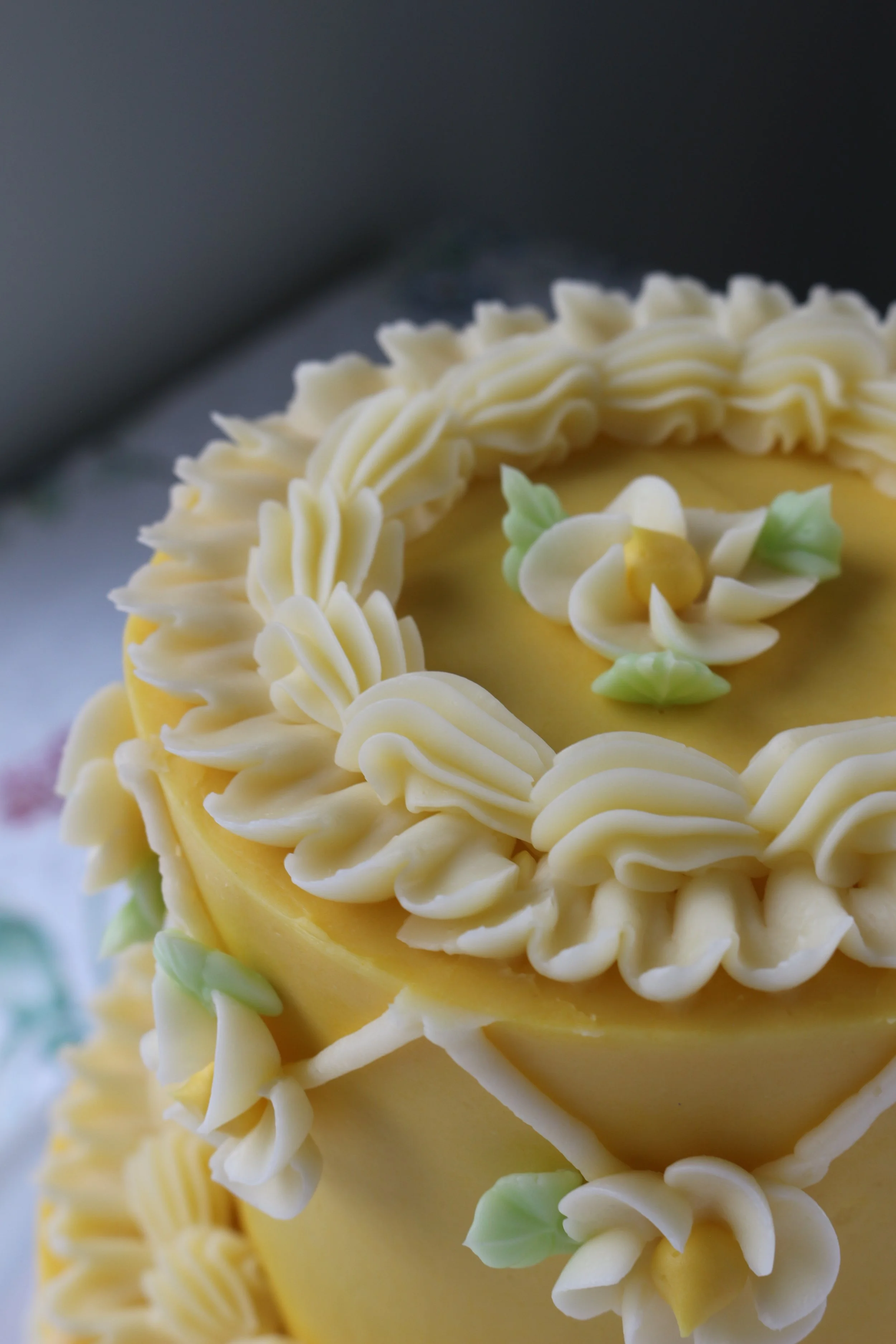 Made by Cakes by Caroline. Close-up of wo-tiered yellow cake with geometric, floral, ruffle, and shell designs.
