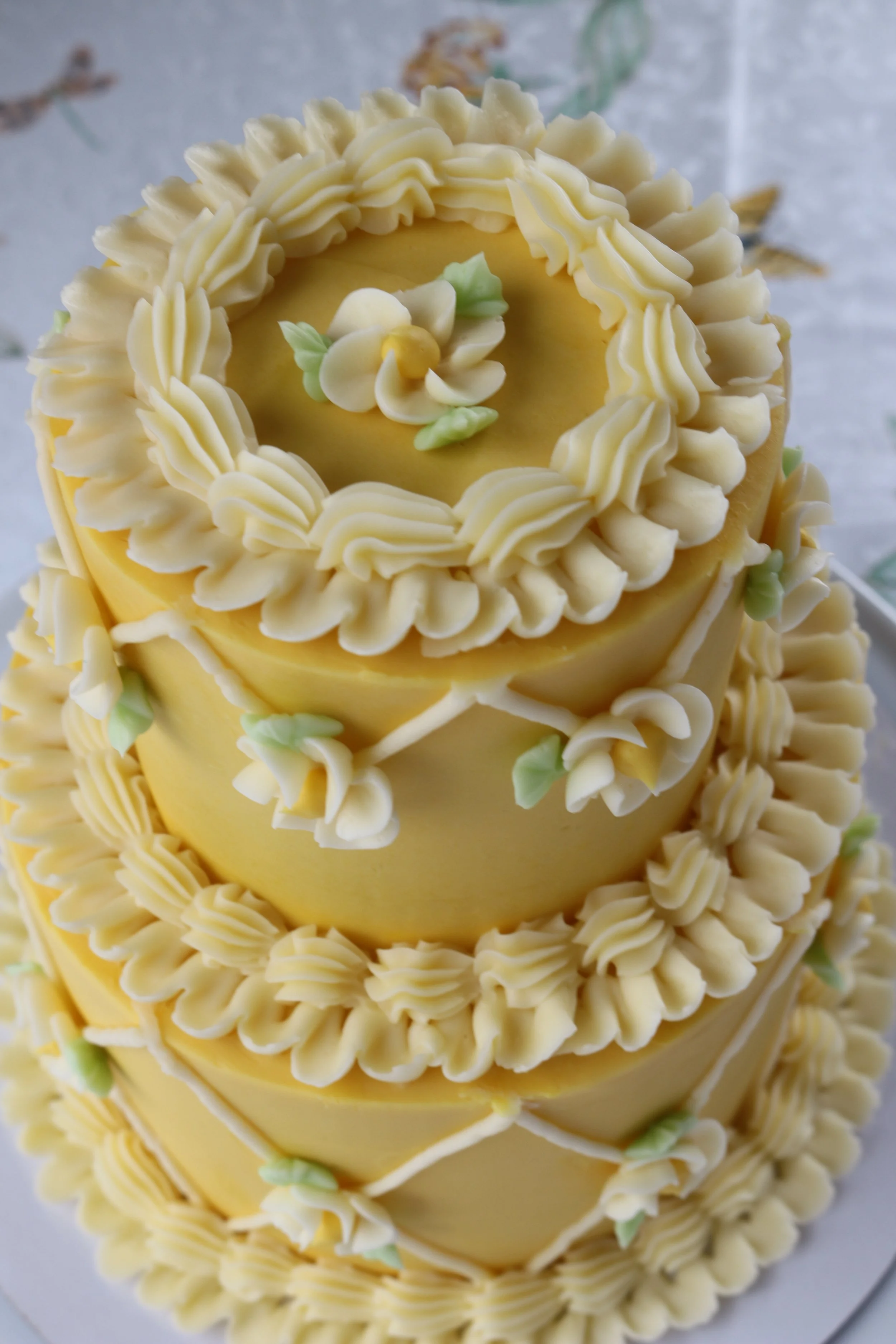Made by Cakes by Caroline. Two-tiered yellow cake with geometric, floral, ruffle, and shell designs.