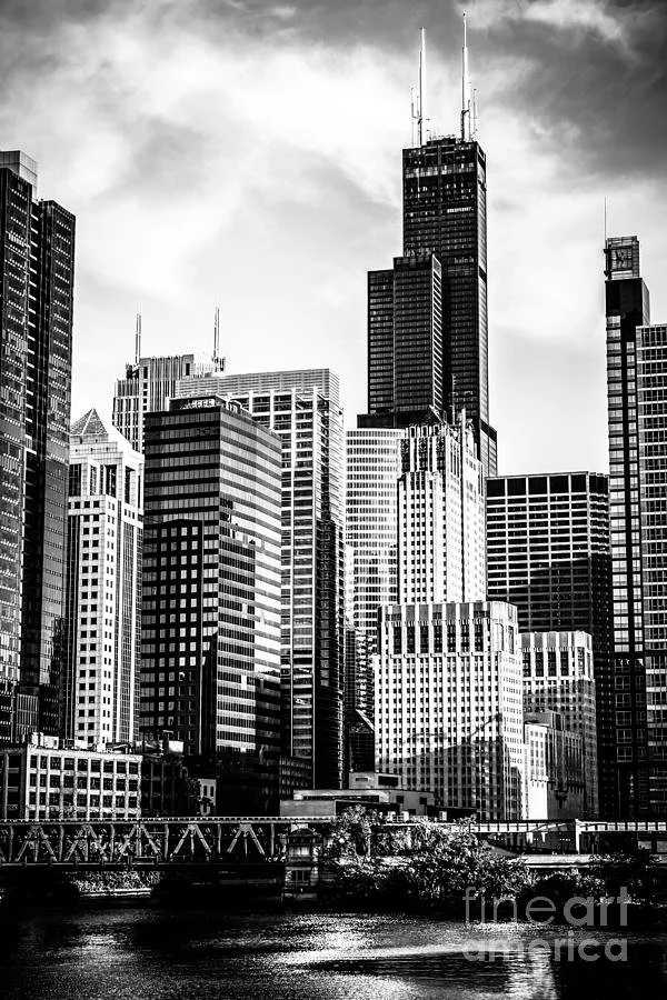 Black and white photo of a Chicago city skyline with tall skyscrapers and the Chicago River in the foreground.
