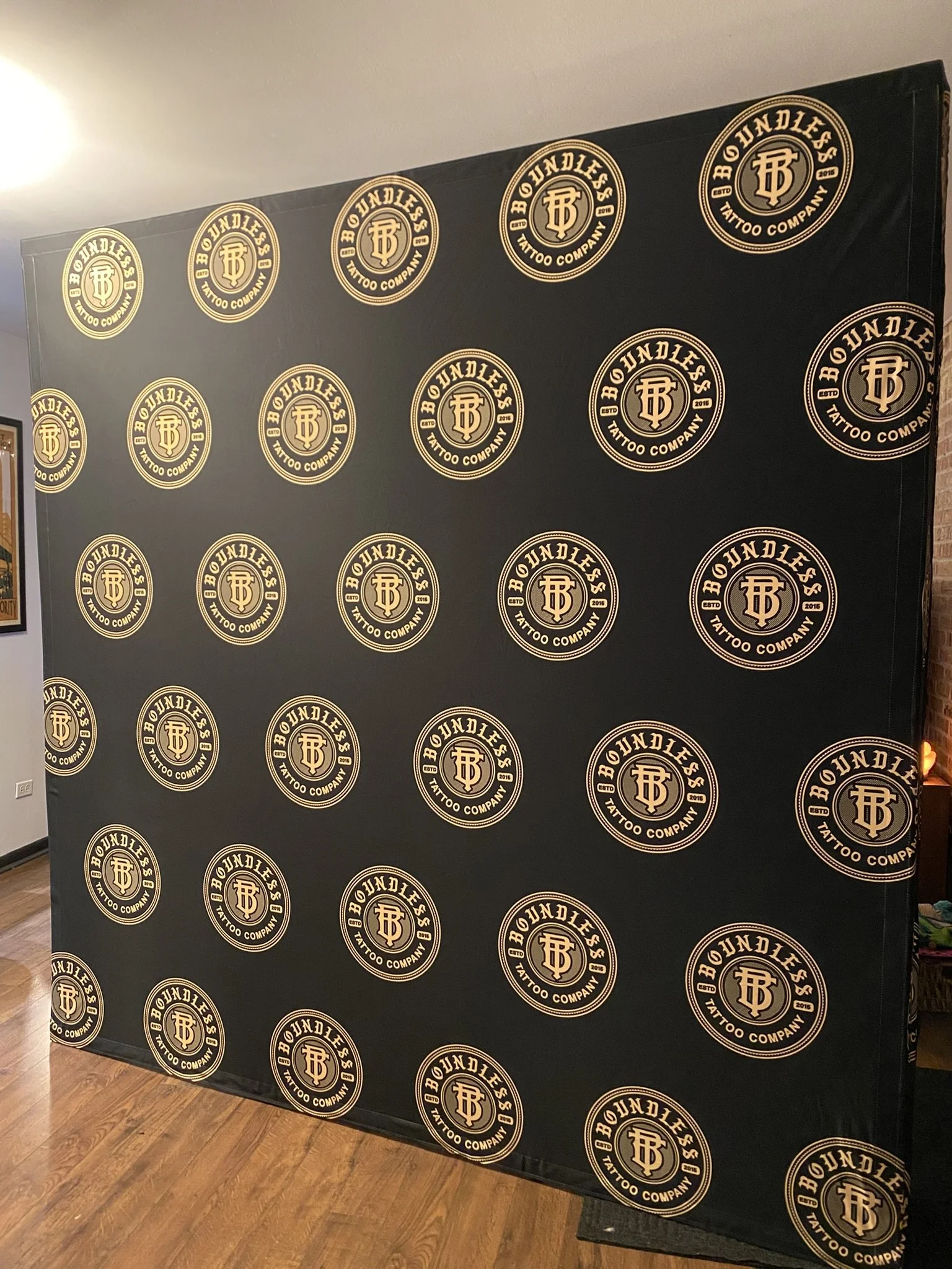 Black wall with multiple round gold and black stickers for 'BONDLESS TATTOO COMPANY' arranged in a grid pattern.