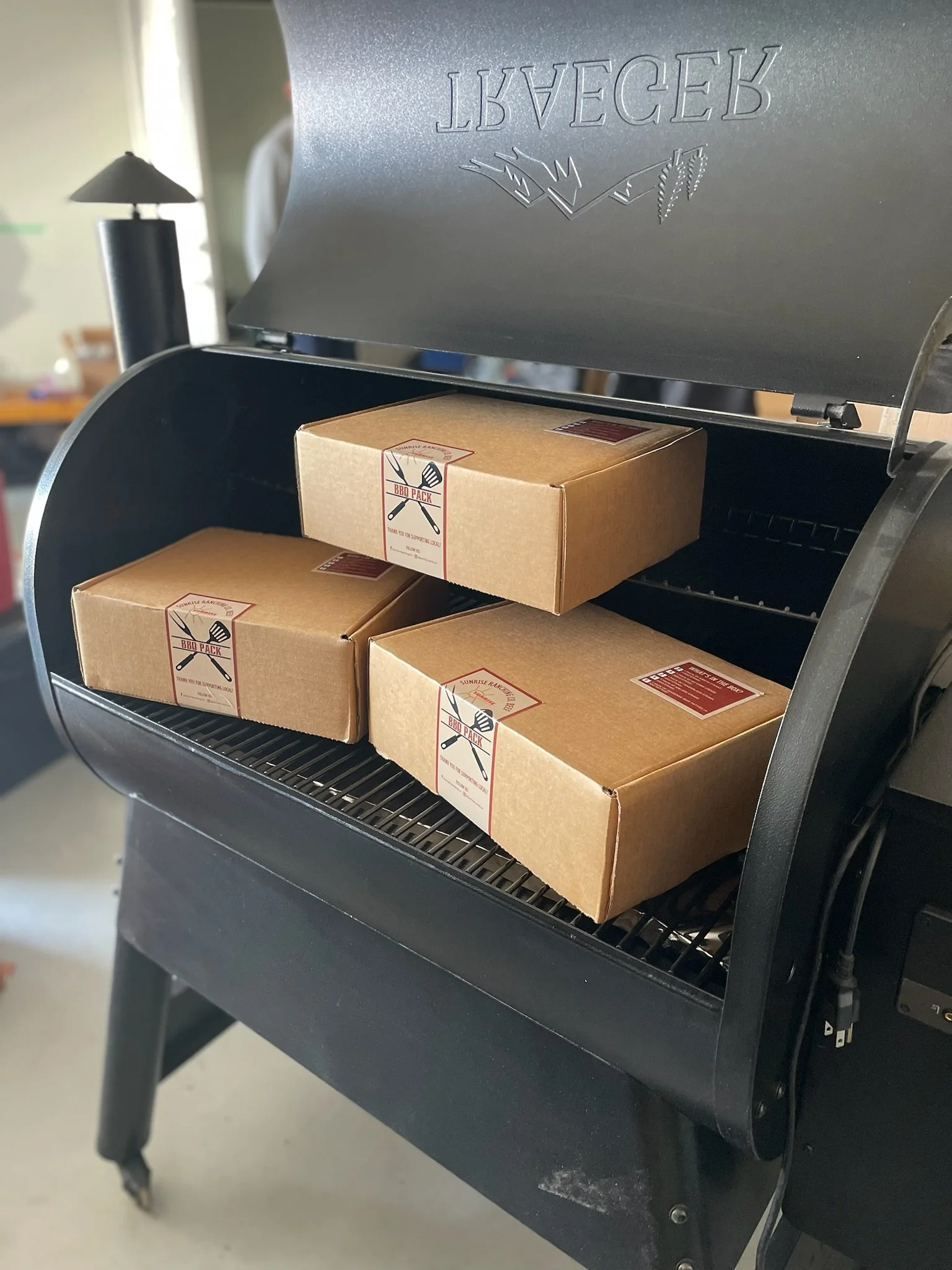 Three cardboard boxes labeled 'BBQ PACK' inside a black smoker grill.