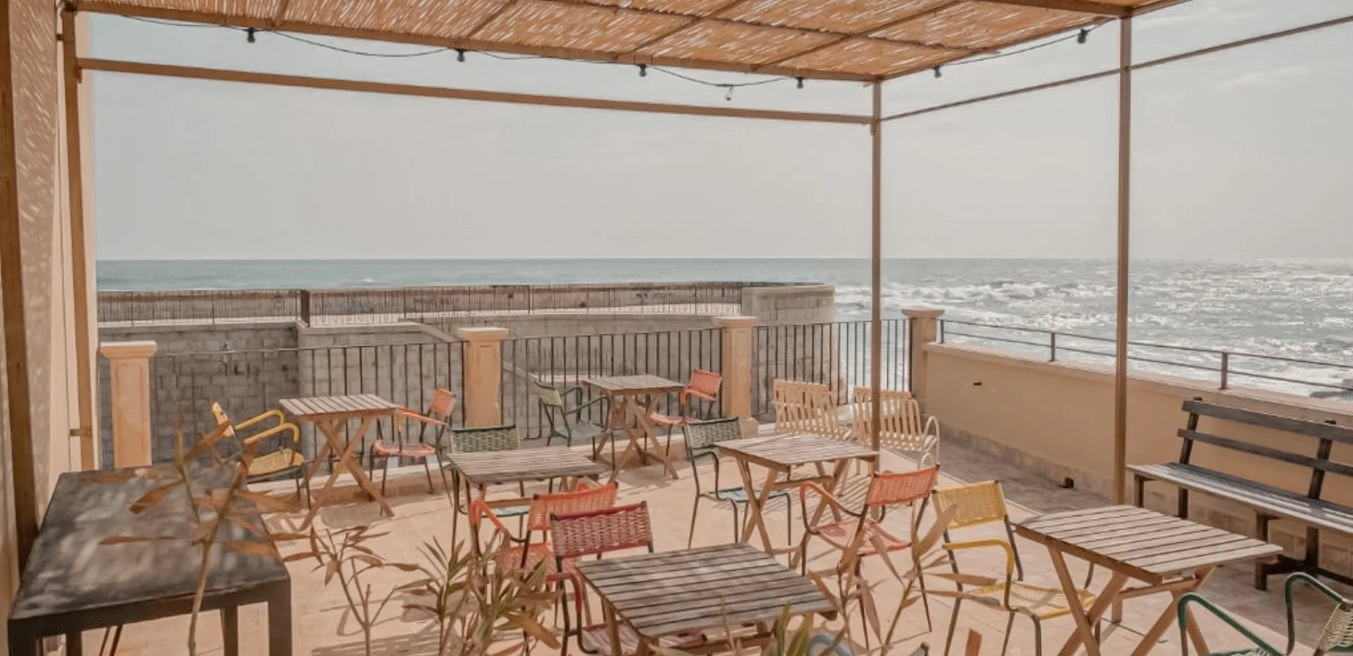 Beachside outdoor seating area with wooden tables and chairs, overlooking the ocean on a cloudy day.