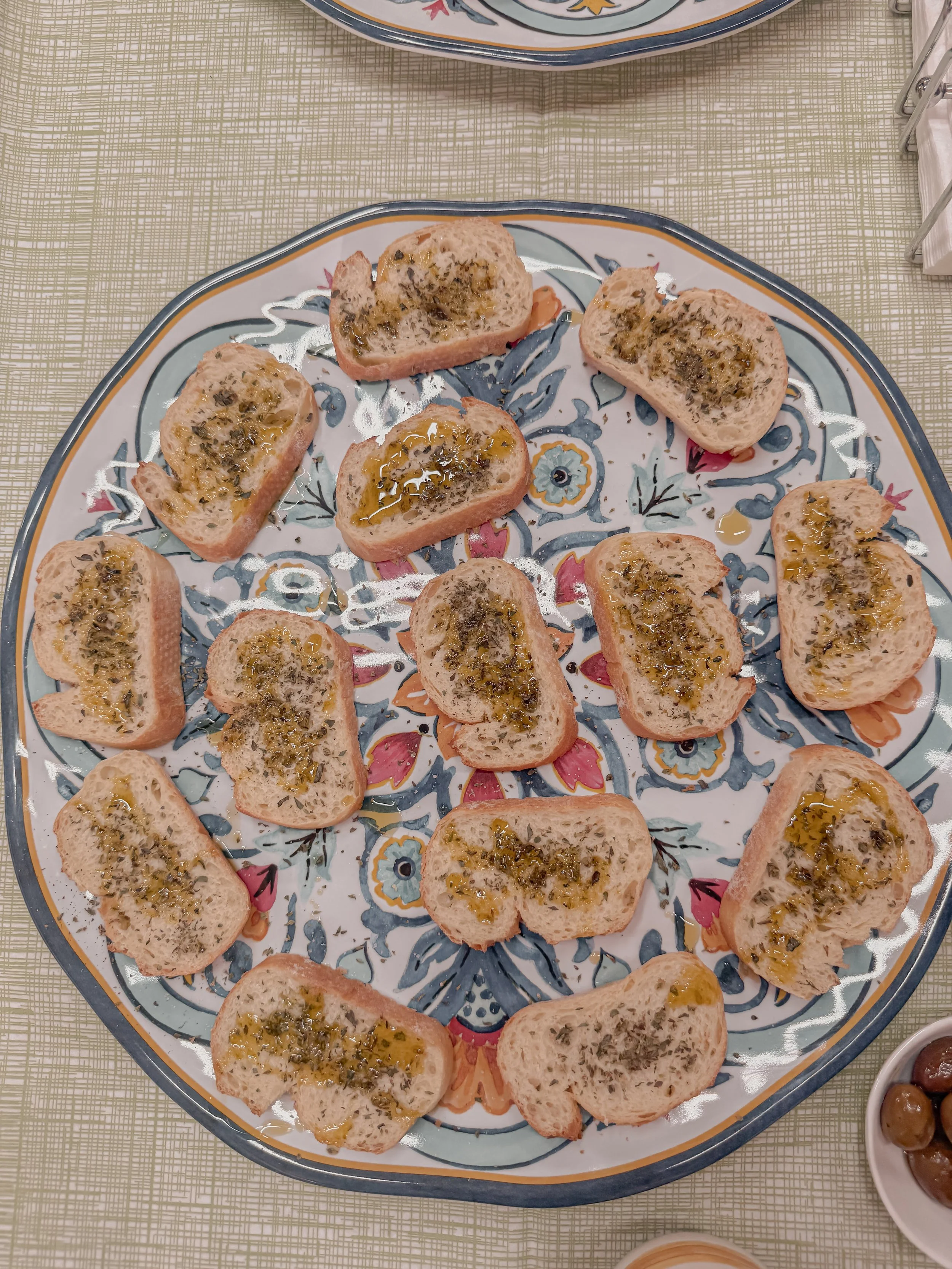 Slices of bread topped with herbs and olive oil on a decorative plate