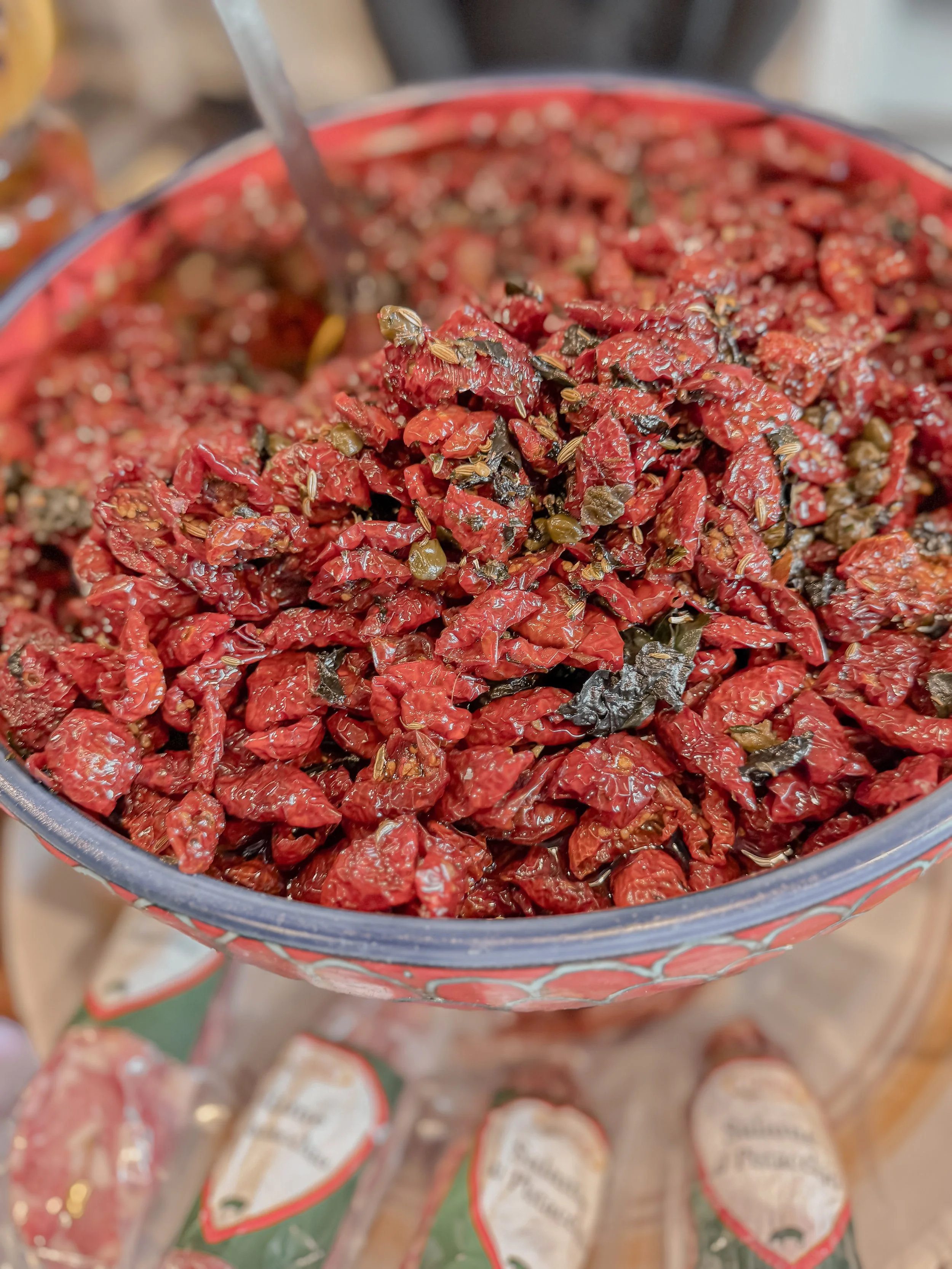 Close-up of a red and green jar filled with sun-dried tomatoes and herbs.